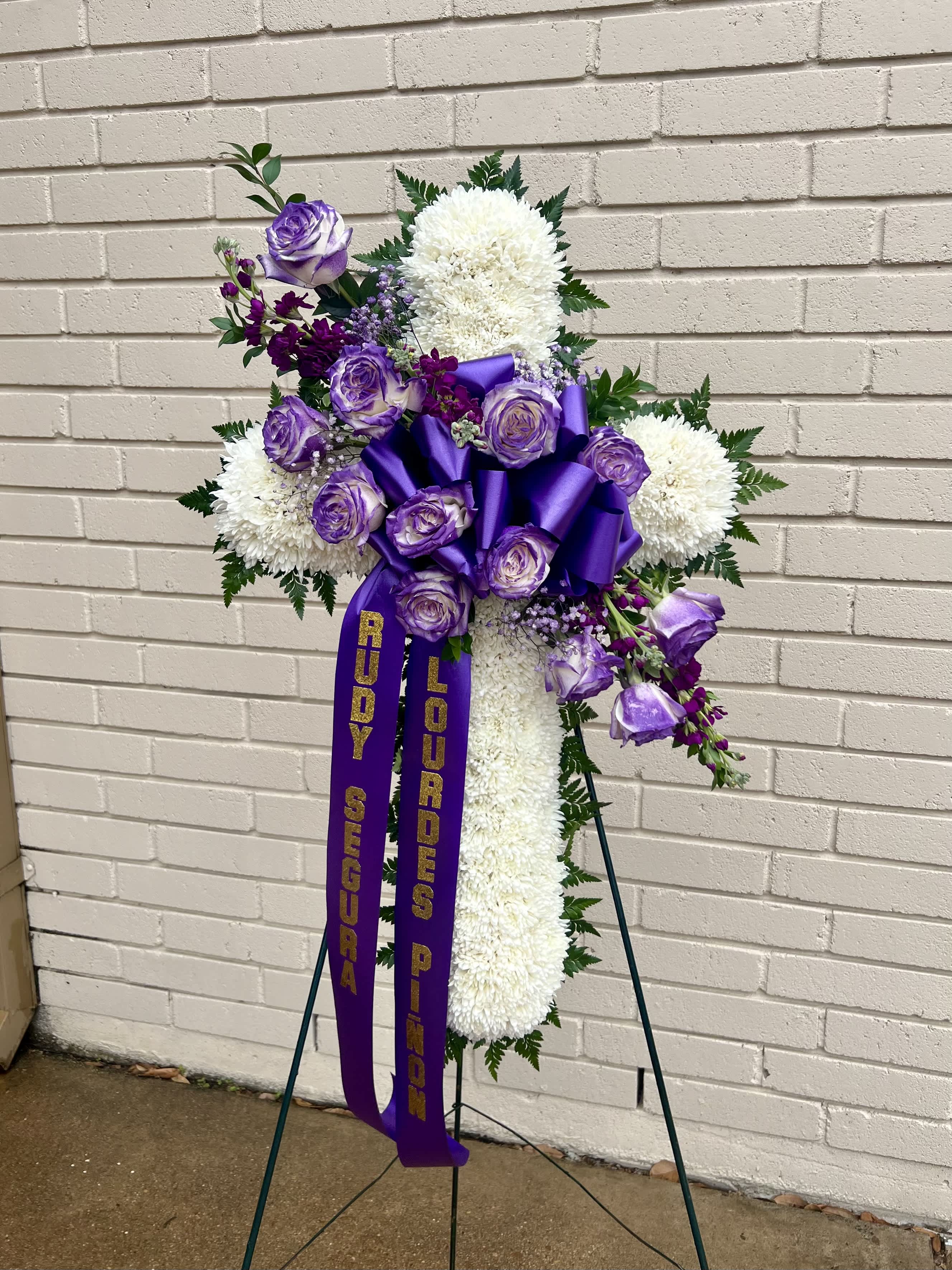 Purple and white funeral spray on a stand with ribbons