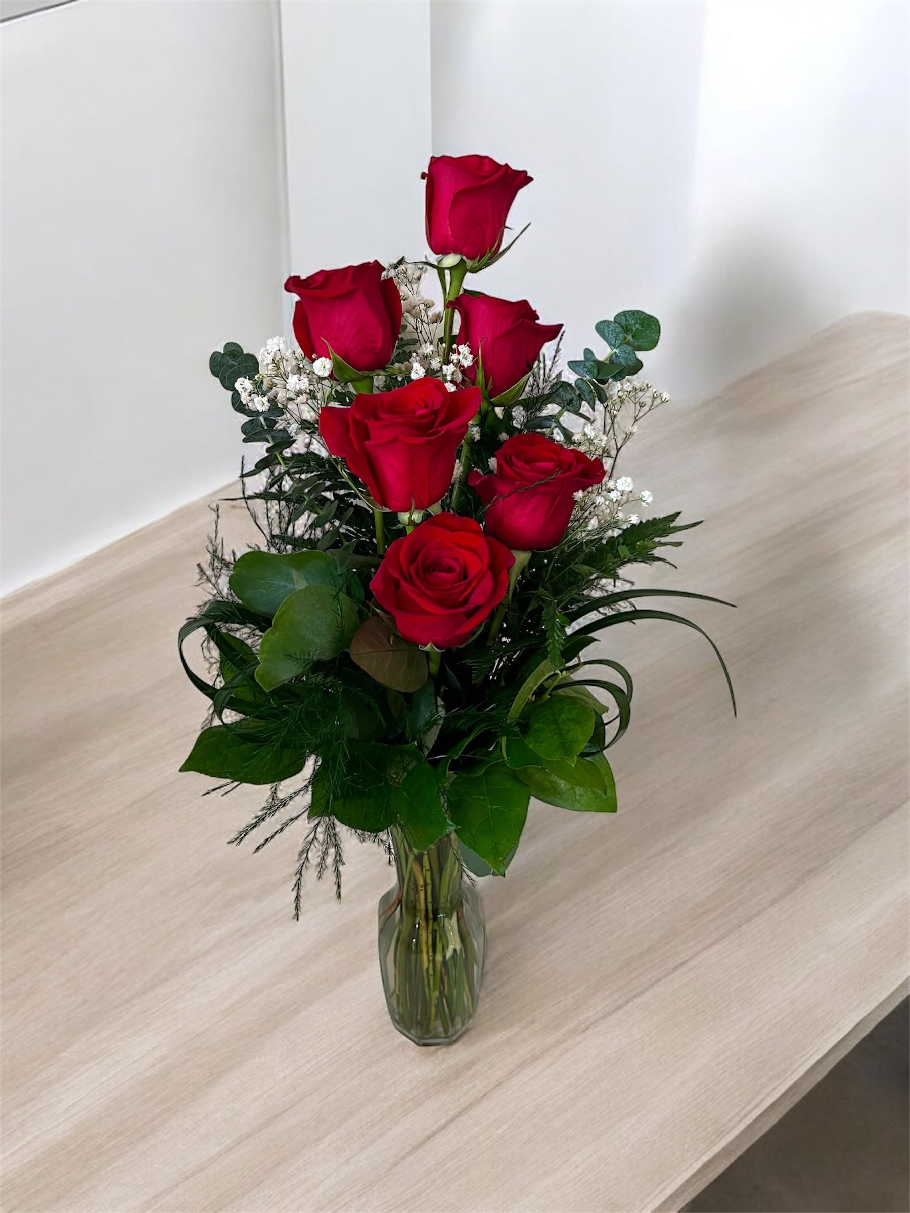 Red roses arranged in a clear glass vase with white filler flowers