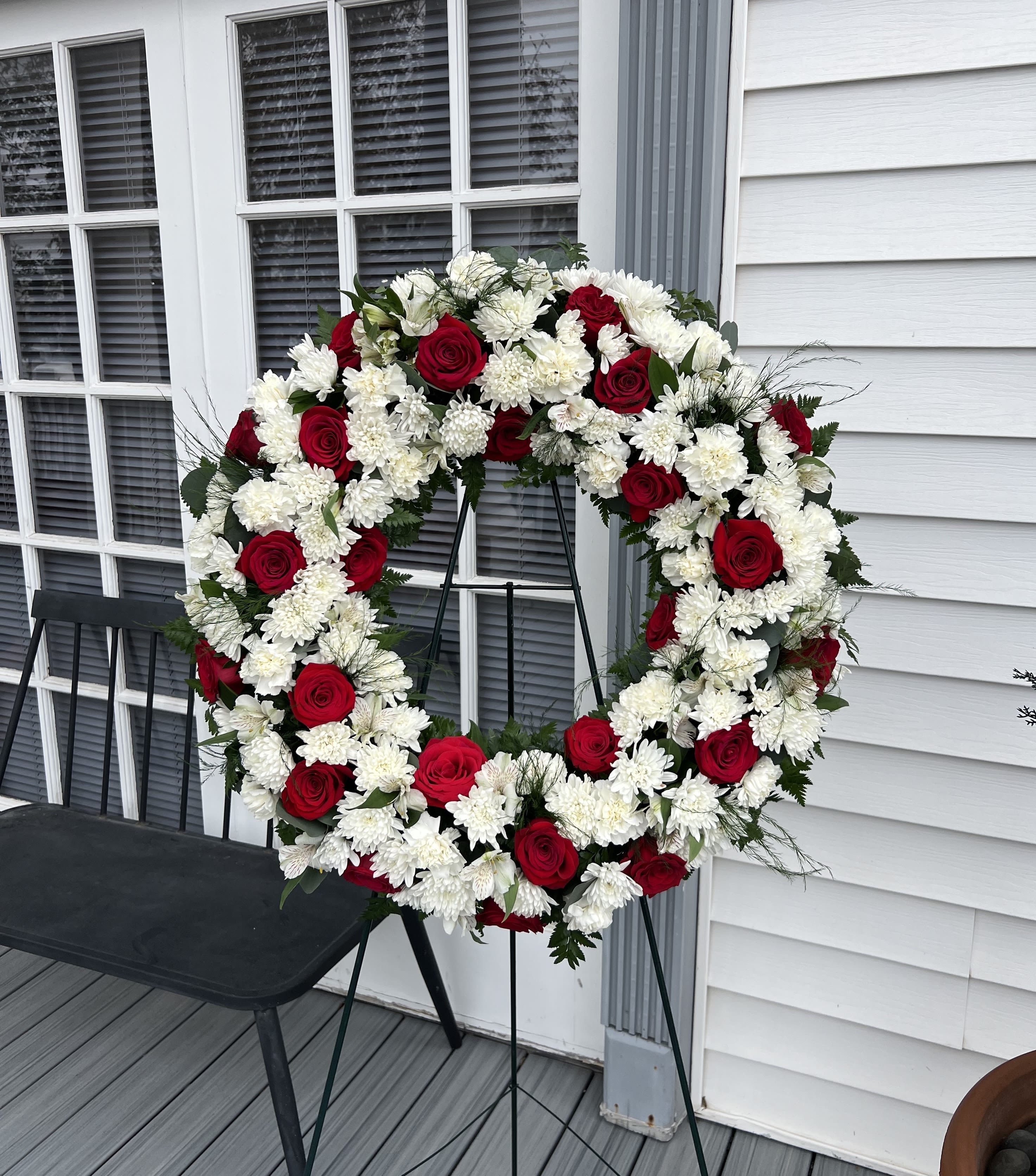 Red roses and white chrysanthemums arranged in a large wreath on a stand
