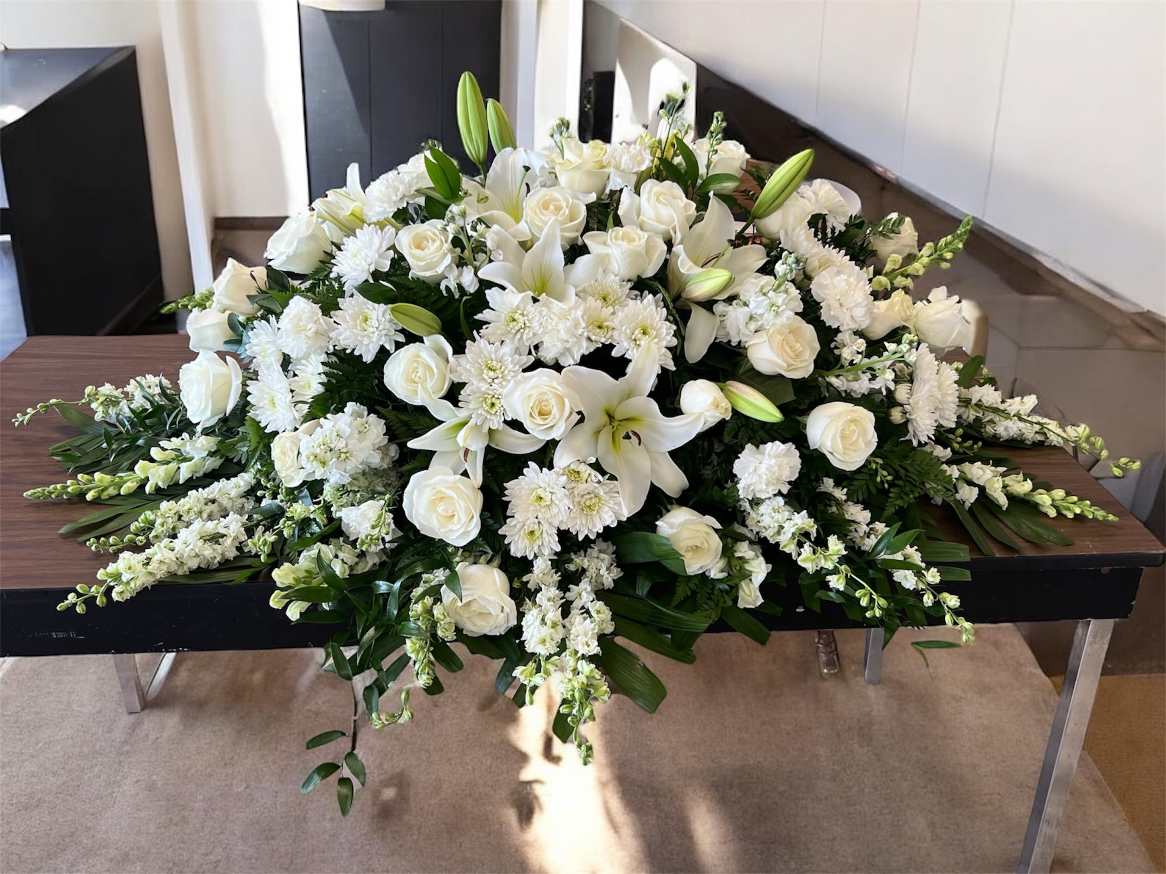 White floral casket spray with roses, lilies, and chrysanthemums