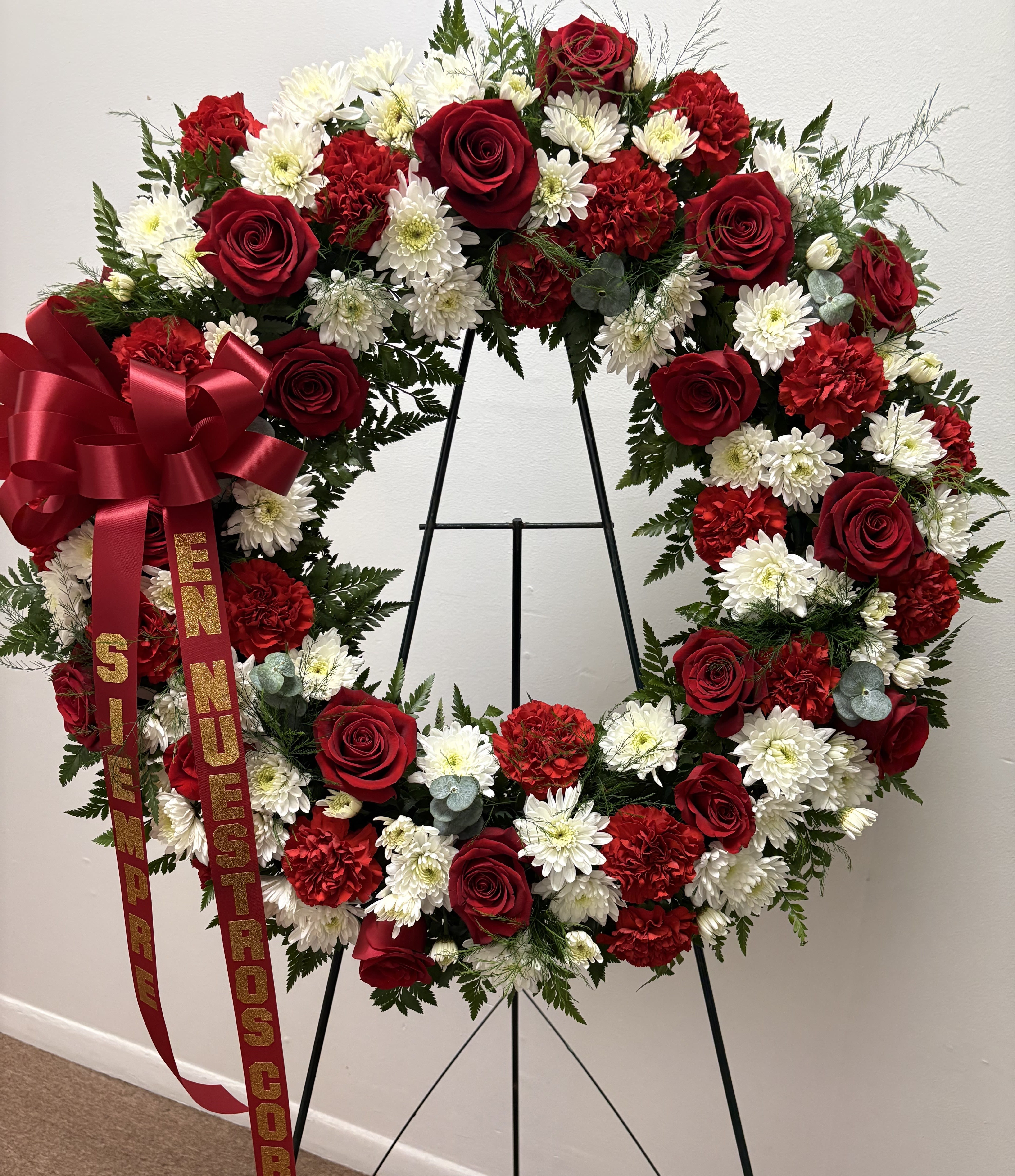 Heart-shaped wreath of red roses, white daisies, and red carnations on an easel