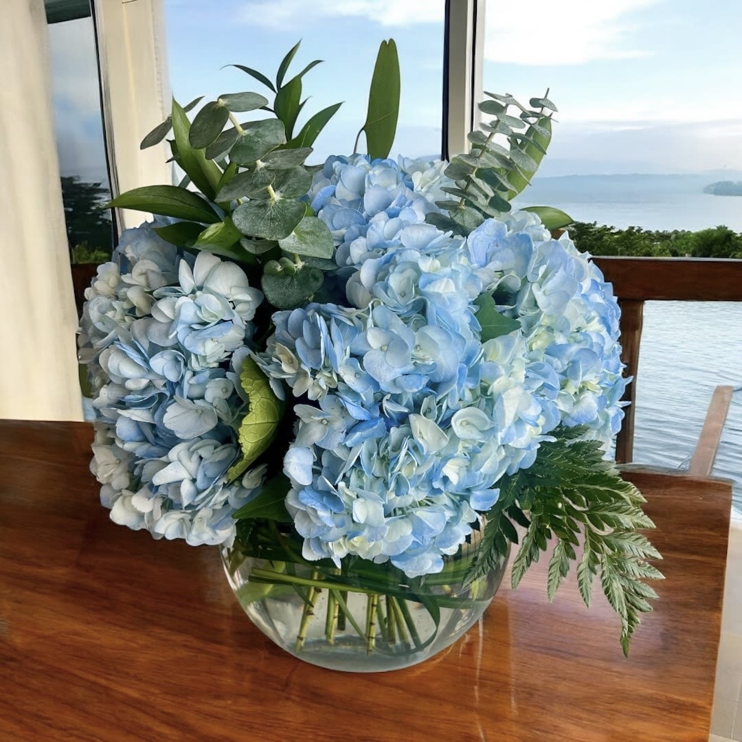 Blue hydrangea arrangement in a clear glass bowl vase