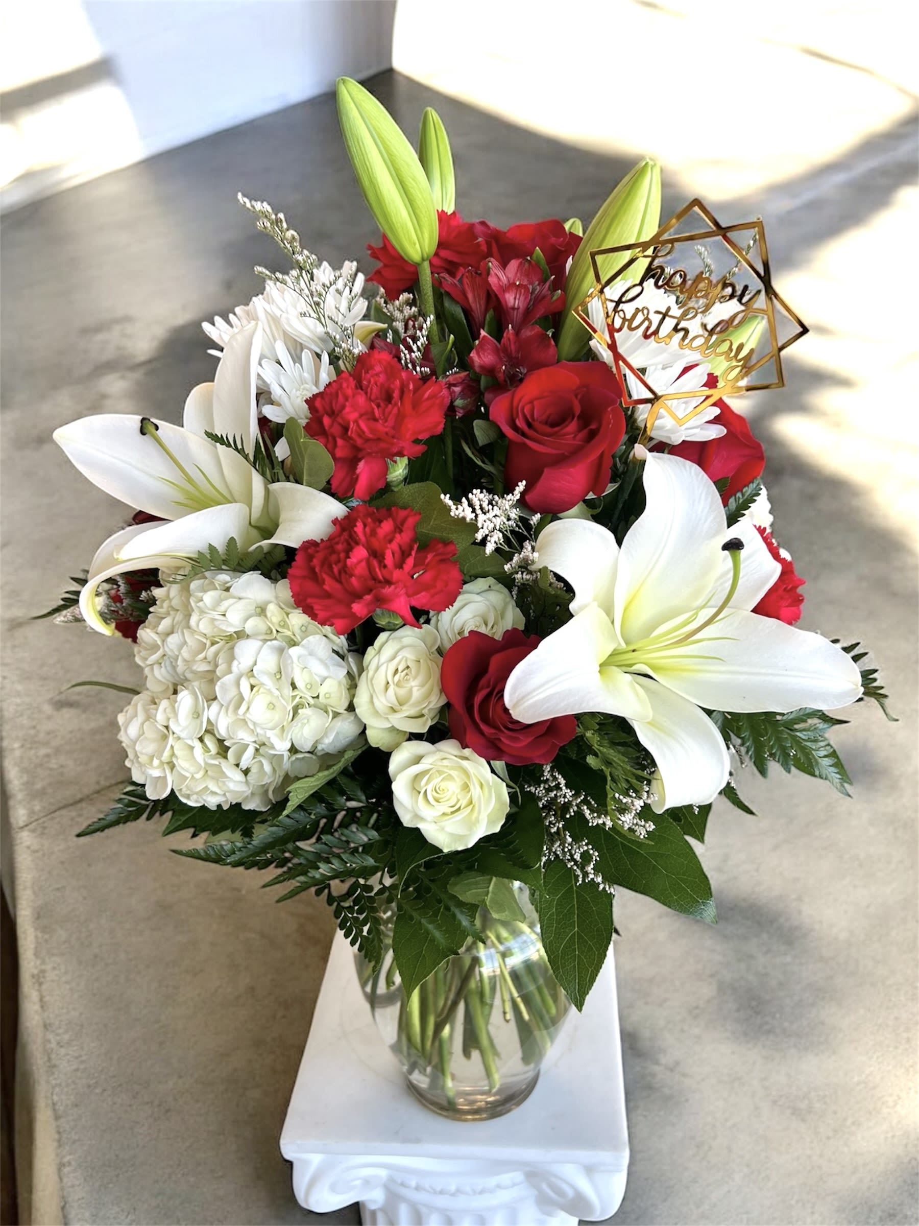 Red and white bouquet with lilies, roses, and a birthday topper in a glass vase