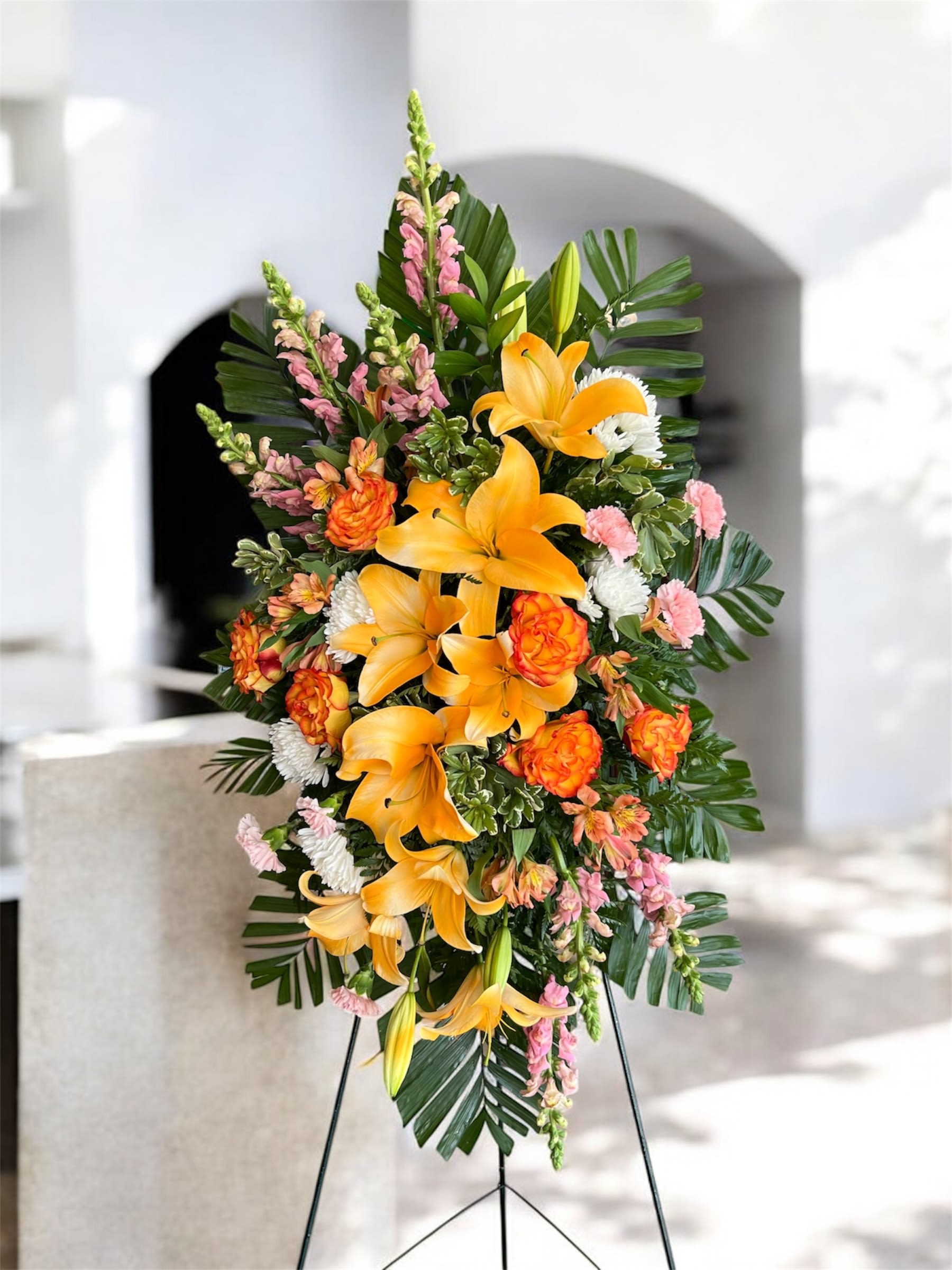 Standing floral spray with orange lilies and pink blooms on a metal easel