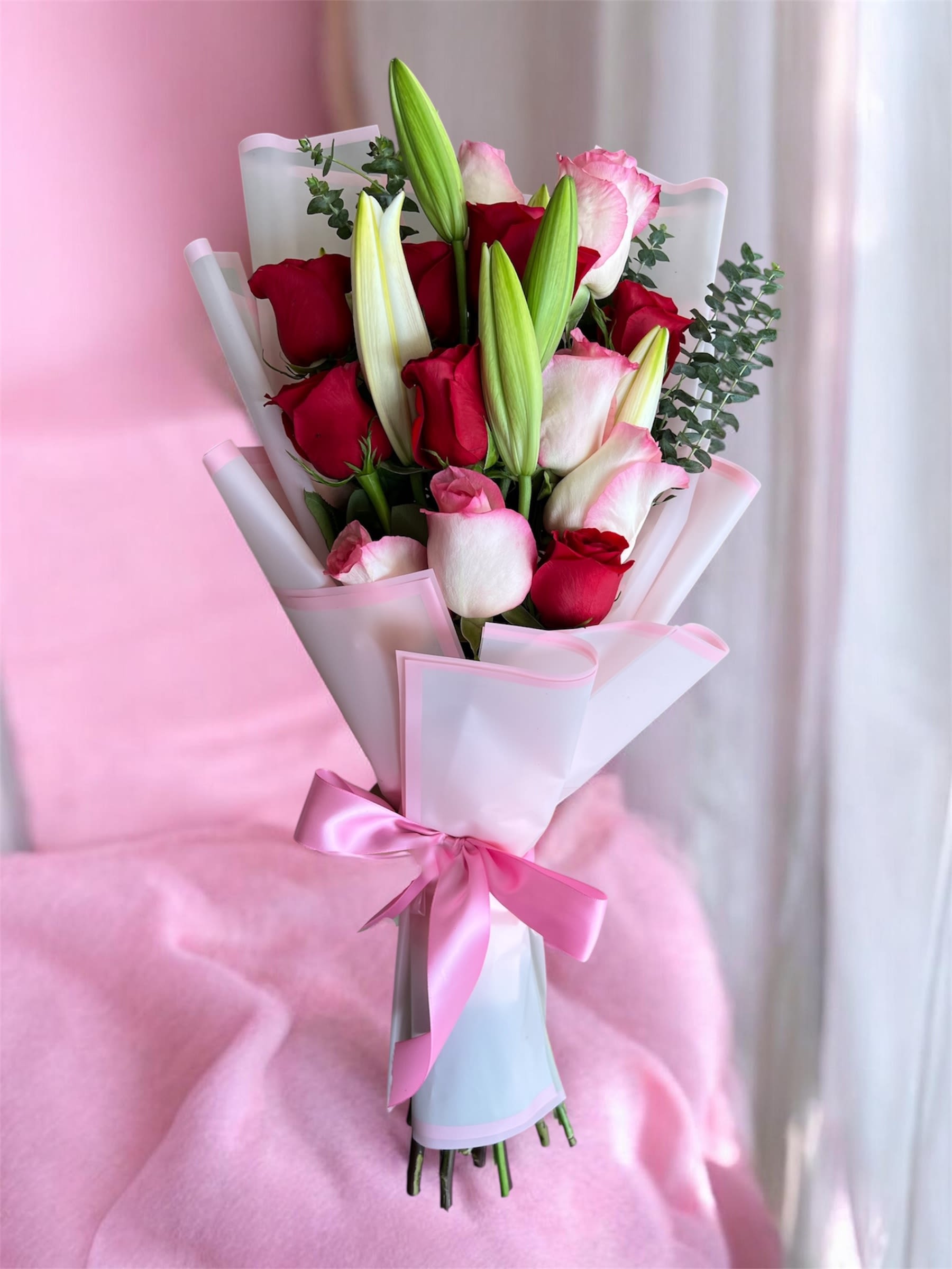Bouquet of red and pink roses with lily buds wrapped in pink paper