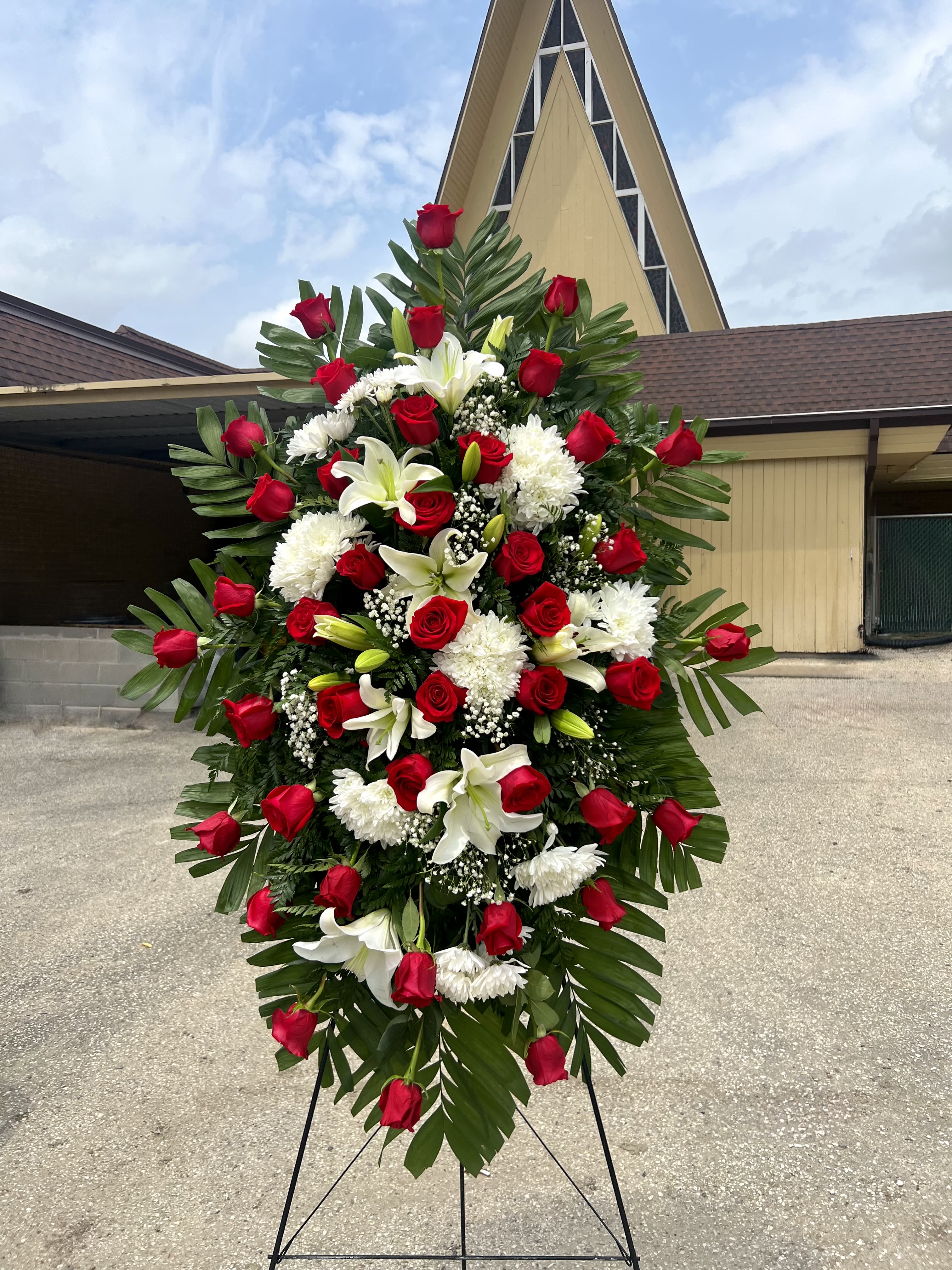 Grand Red and White Standing Spray  - A lush, formal standing spray that reads with ceremonial grace - perfect as a sympathy arrangement or memorial tribute. The Grand Red and White standing spray pairs deep red roses and crisp white lilies to create a heartfelt message of love and remembrance, the kind of floral tribute that helps the person you're honoring feel genuinely seen and respected.