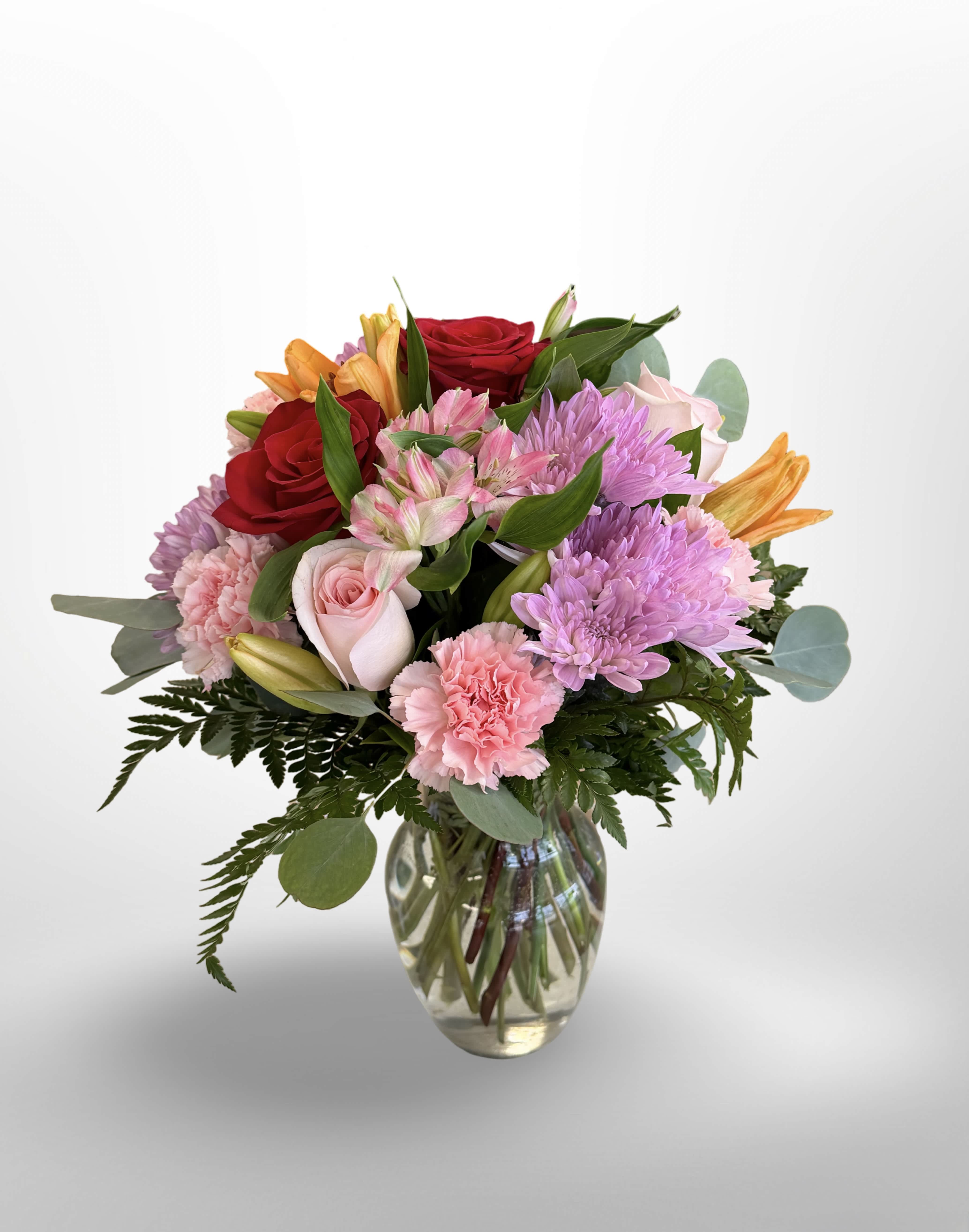 Mixed bouquet of roses, lilies, carnations, and chrysanthemums in a glass vase