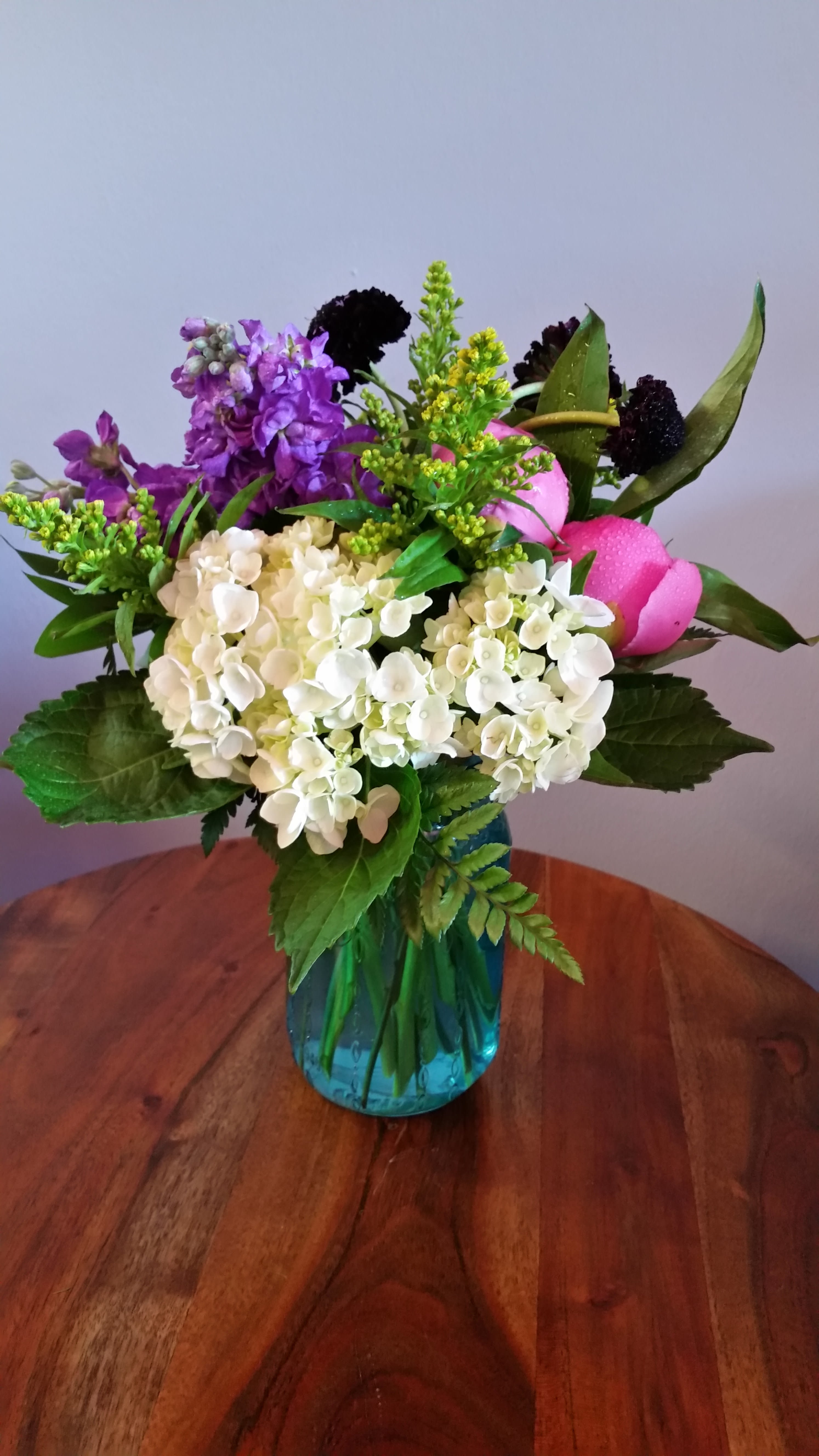 Mixed bouquet of white hydrangeas, purple blooms, and pink tulips in a blue vase