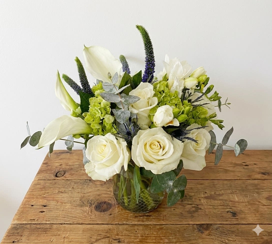 White roses and calla lilies in a glass vase with green and purple accents