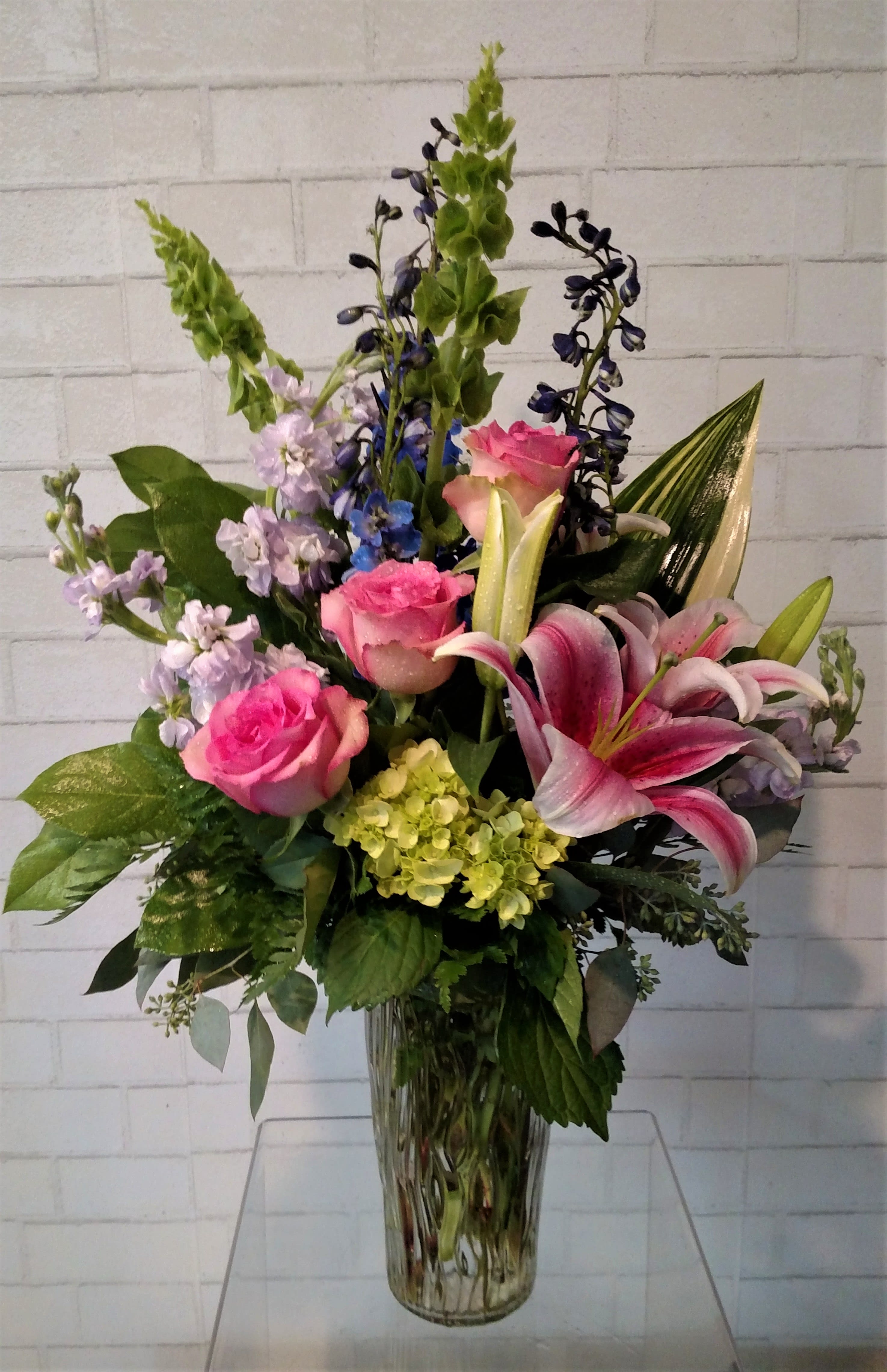 Pink roses and lilies in a clear glass vase with mixed purple blooms