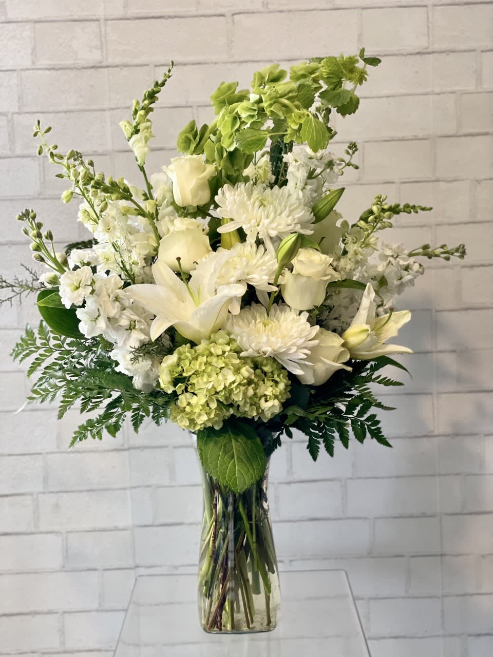 White floral arrangement in a clear glass vase with lilies, roses, and chrysanthemums
