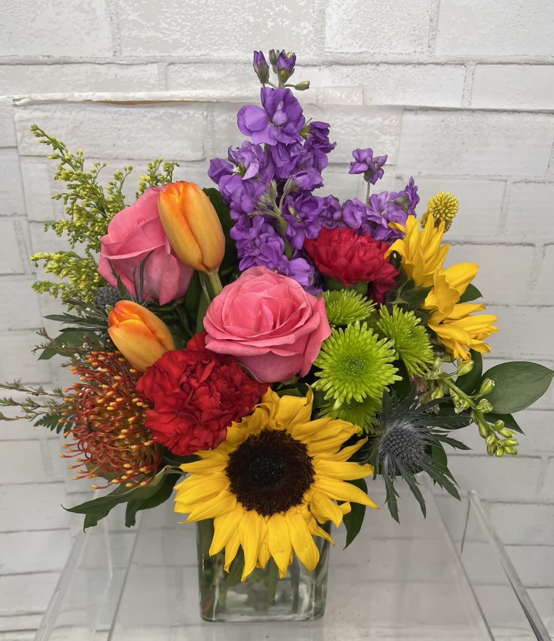 Mixed bouquet with roses, tulips, sunflowers, and purple blooms in a glass vase