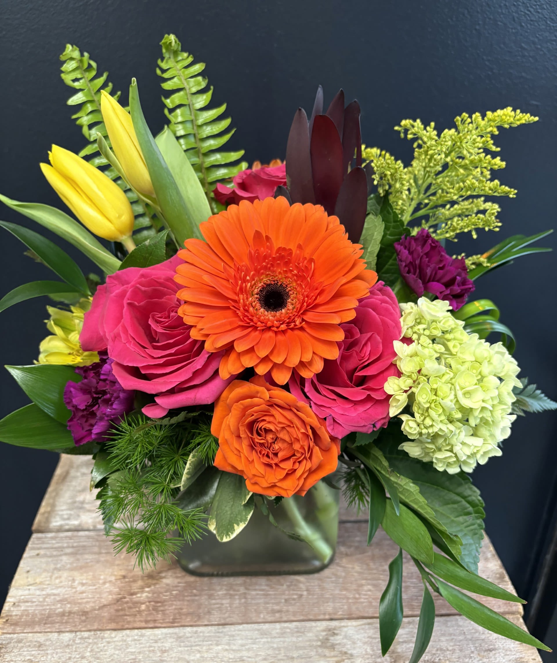 Bright mixed bouquet with orange gerbera, pink roses, and yellow tulips in a glass vase