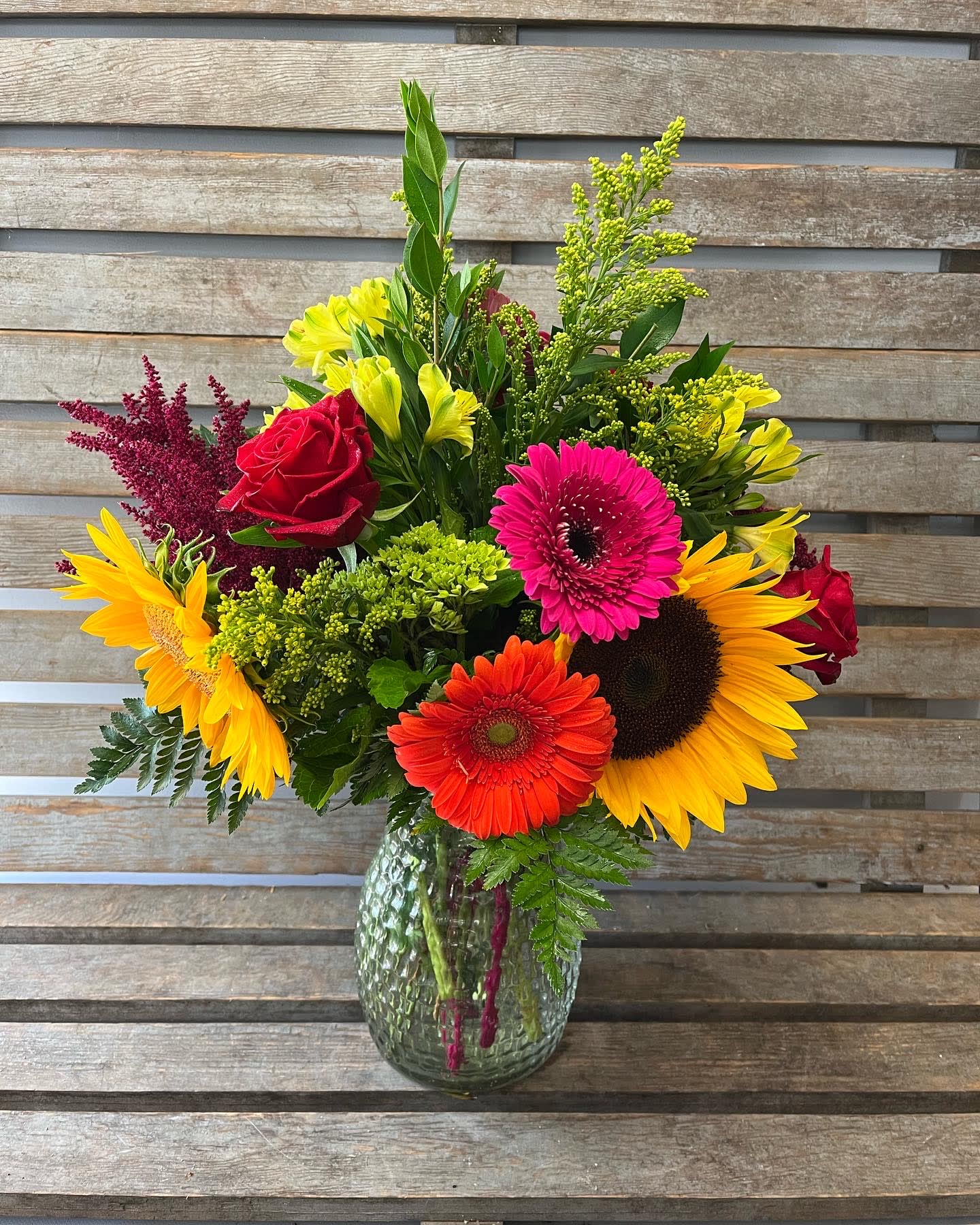Mixed bouquet of sunflowers, gerbera daisies, and roses in a glass vase