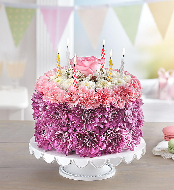 Pink floral cake with striped birthday candles on a white stand