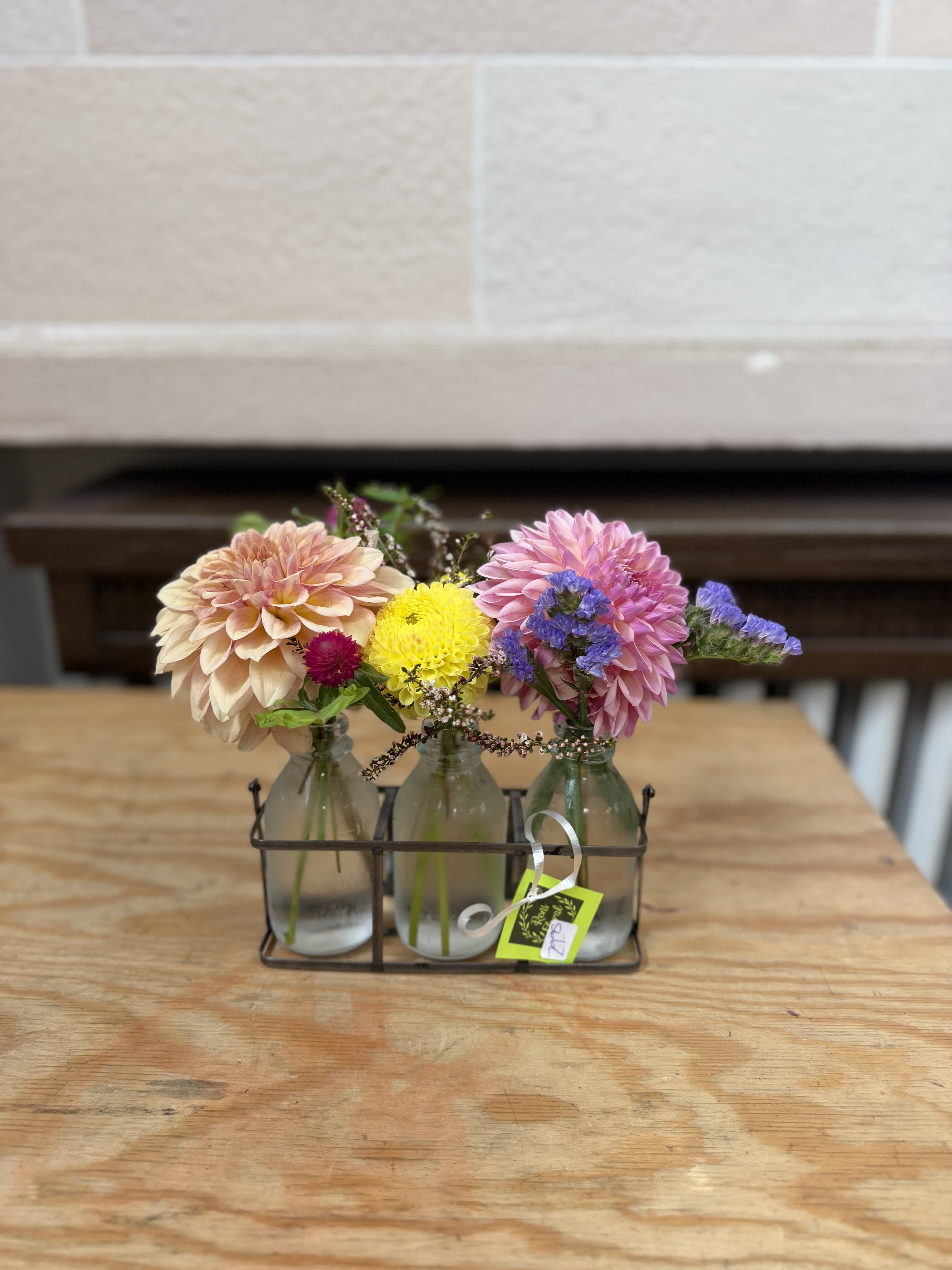 Three small glass bottles hold colorful flowers in a metal caddy.