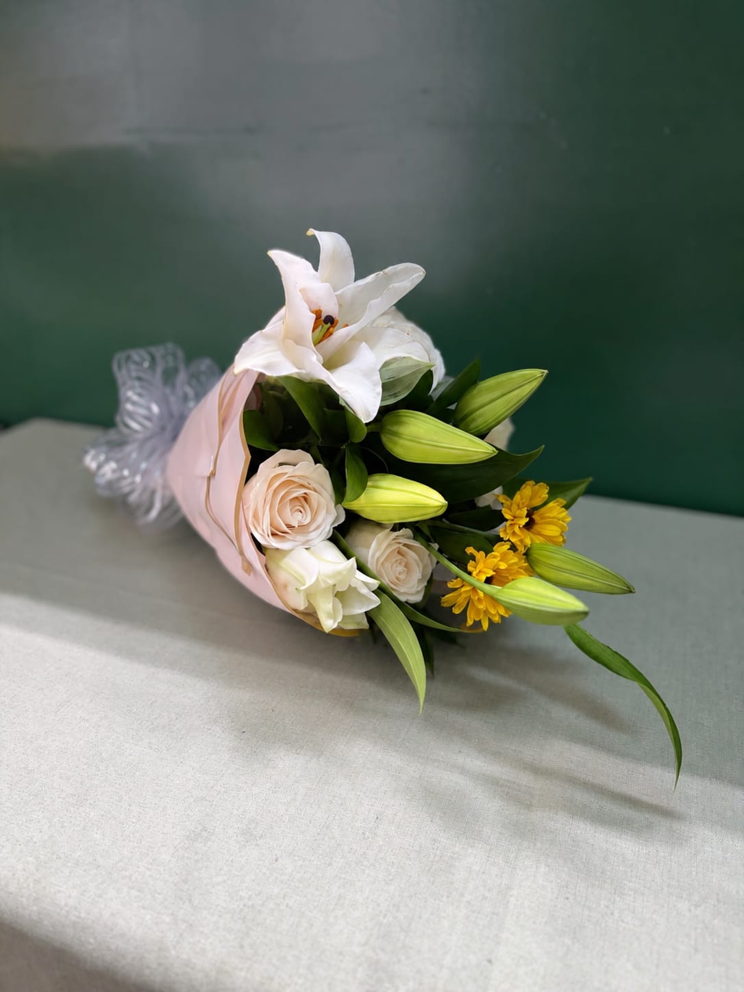 Bouquet of white lilies, pale roses, and yellow flowers wrapped in pink paper