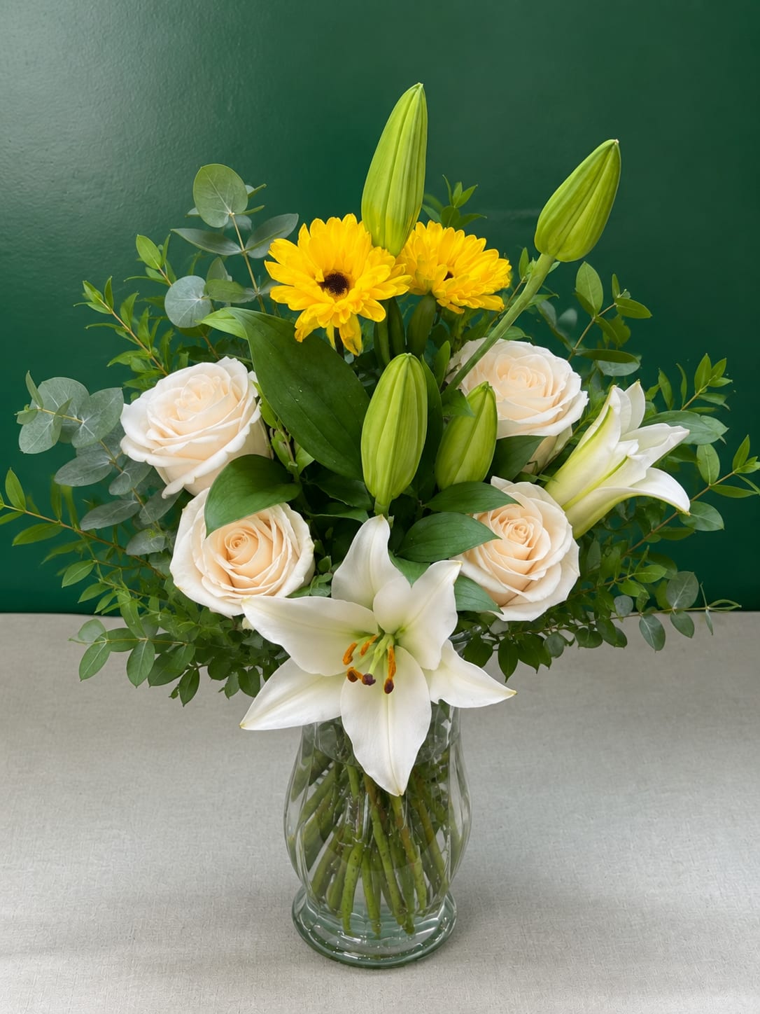White lilies and cream roses in a glass vase with yellow flowers