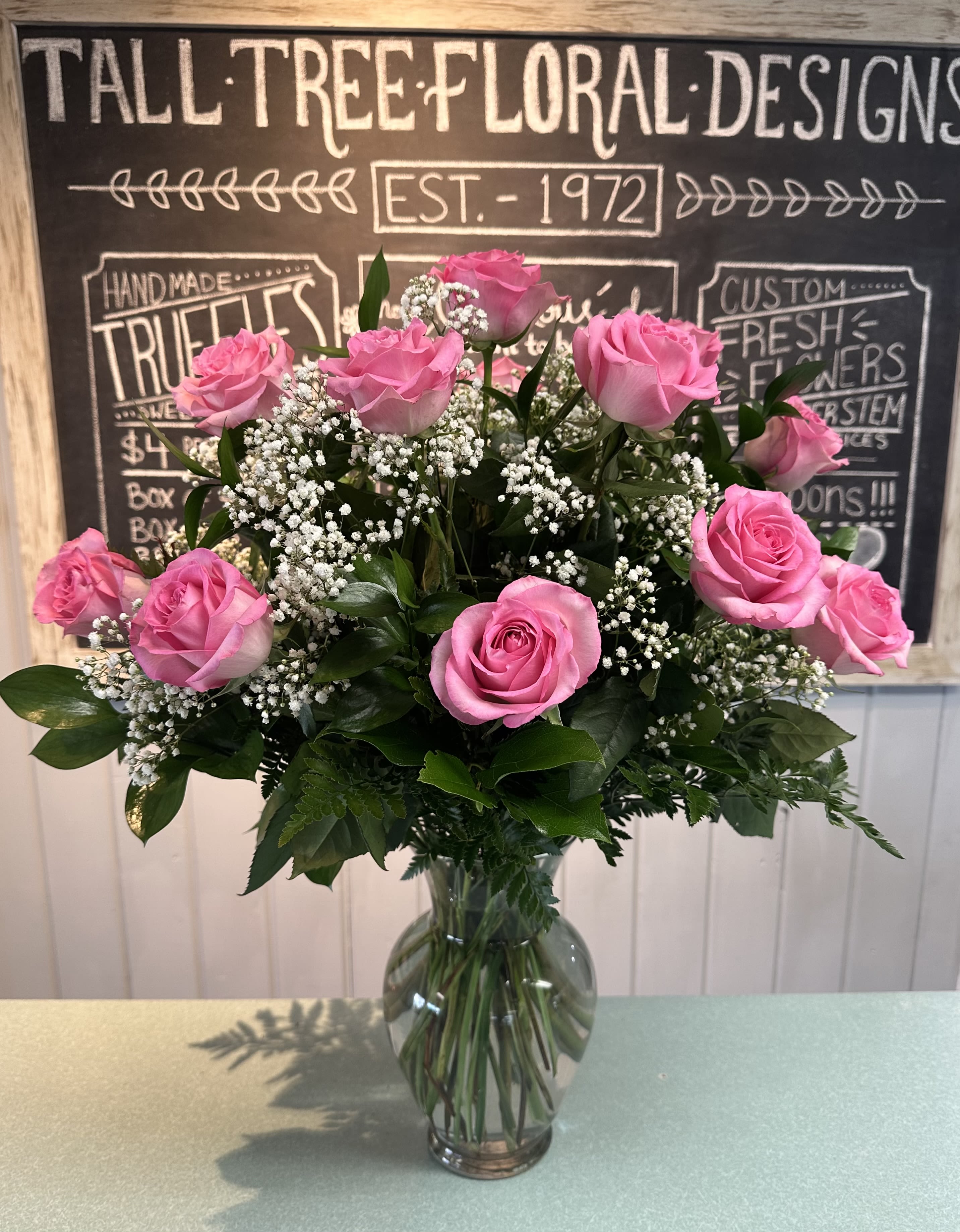 A Dozen Pink Roses  - Pretty pink and perfect. Dozen pink roses, baby's breath and assorted greenery in glass classic urn vase.