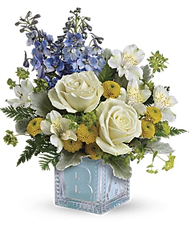 Welcome Little One - White roses, white alstroemeria, yellow button spray chrysanthemums, and blue delphinium are arranged with bupleurum, dusty miller, and leatherleaf fern. Delivered in a Baby Block.