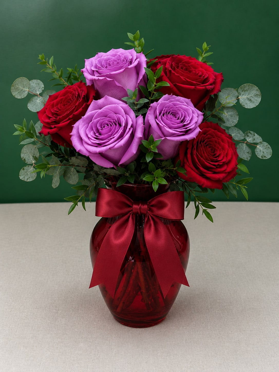Bouquet of red and lavender roses in a red glass vase with a ribbon