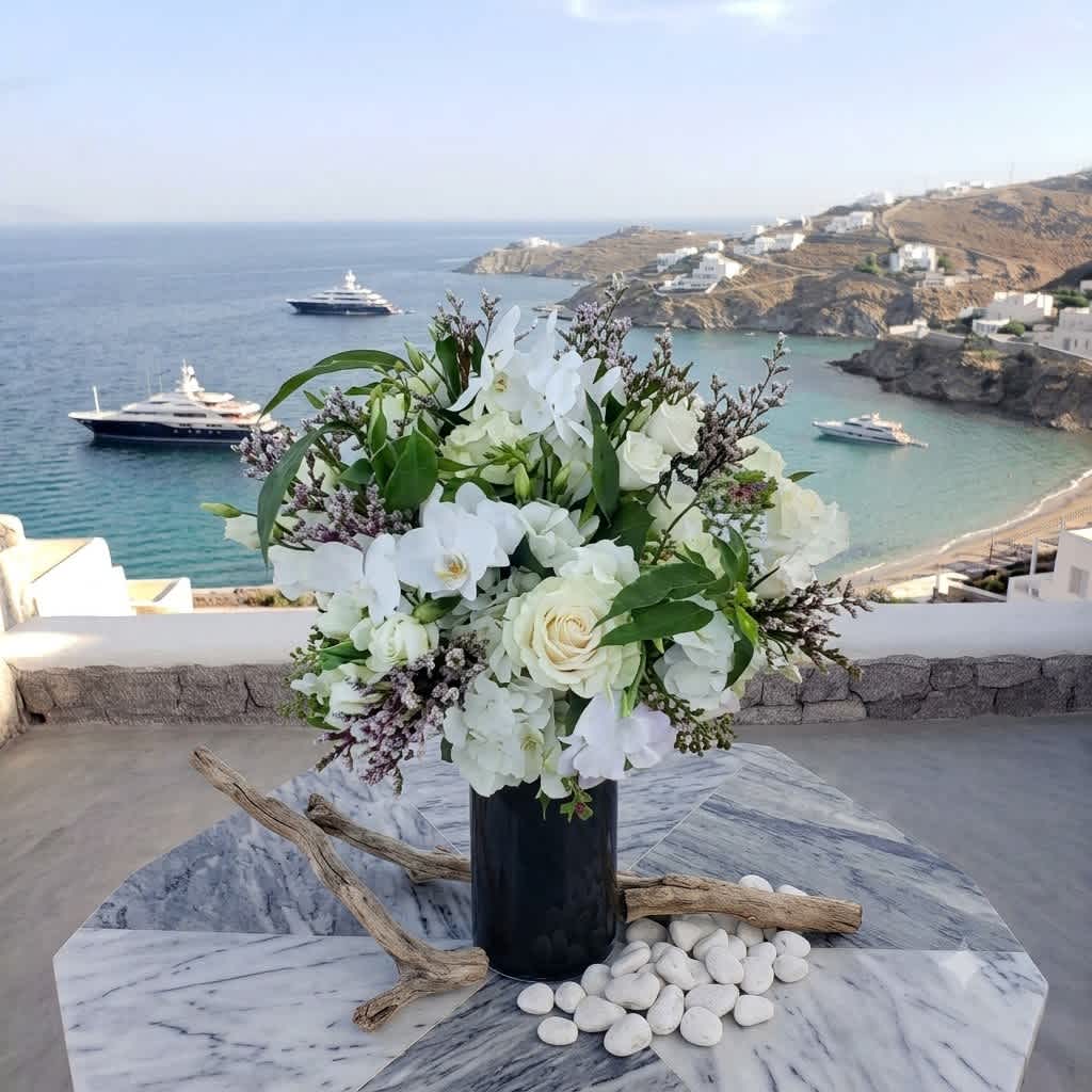 White floral arrangement in a dark vase on a marble table overlooking the sea