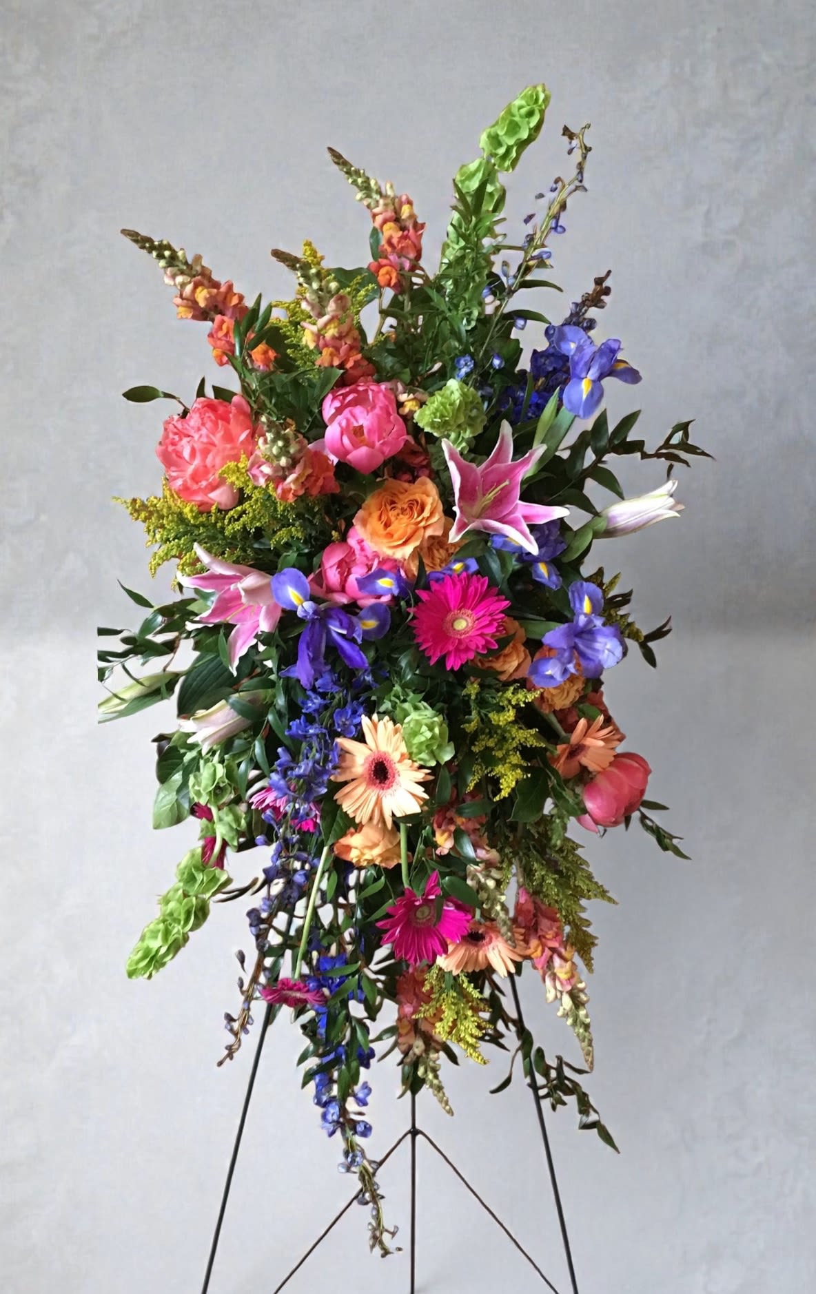 Joyous Garden Easel Spray - Garden style spray in bright pink, purple, orange and green with snapdragons, iris, lilies, gerberas and roses on a metal easel for an uplifting funeral display.