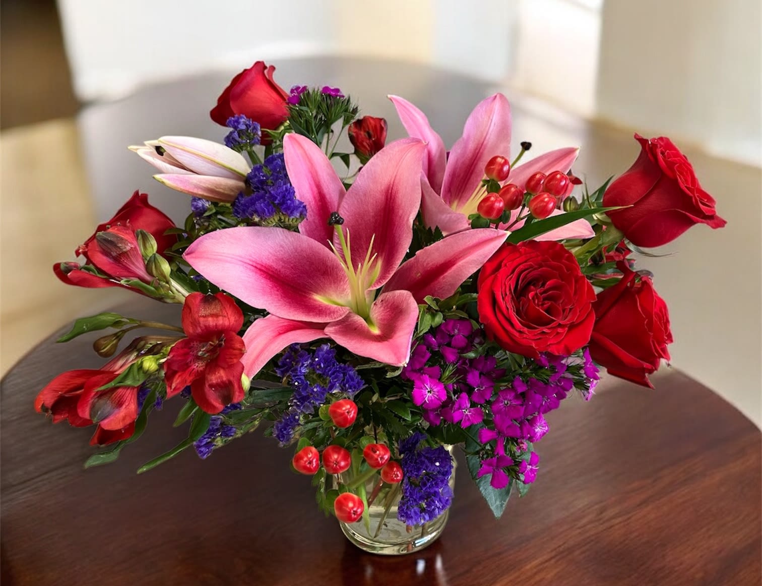 Spicy Love - A bold, spicy arrangement bursting with attitude: fiery red roses and sensual oriental lilies set the tone, while red alstroemeria fans the flame with vibrant energy. Purple sweet William and smoky purple statice add a sultry edge, deep and dramatic. Red hypericum berries pop like sparks throughout the design. Creating a wild, untamed bouquet, impossible to ignore. 