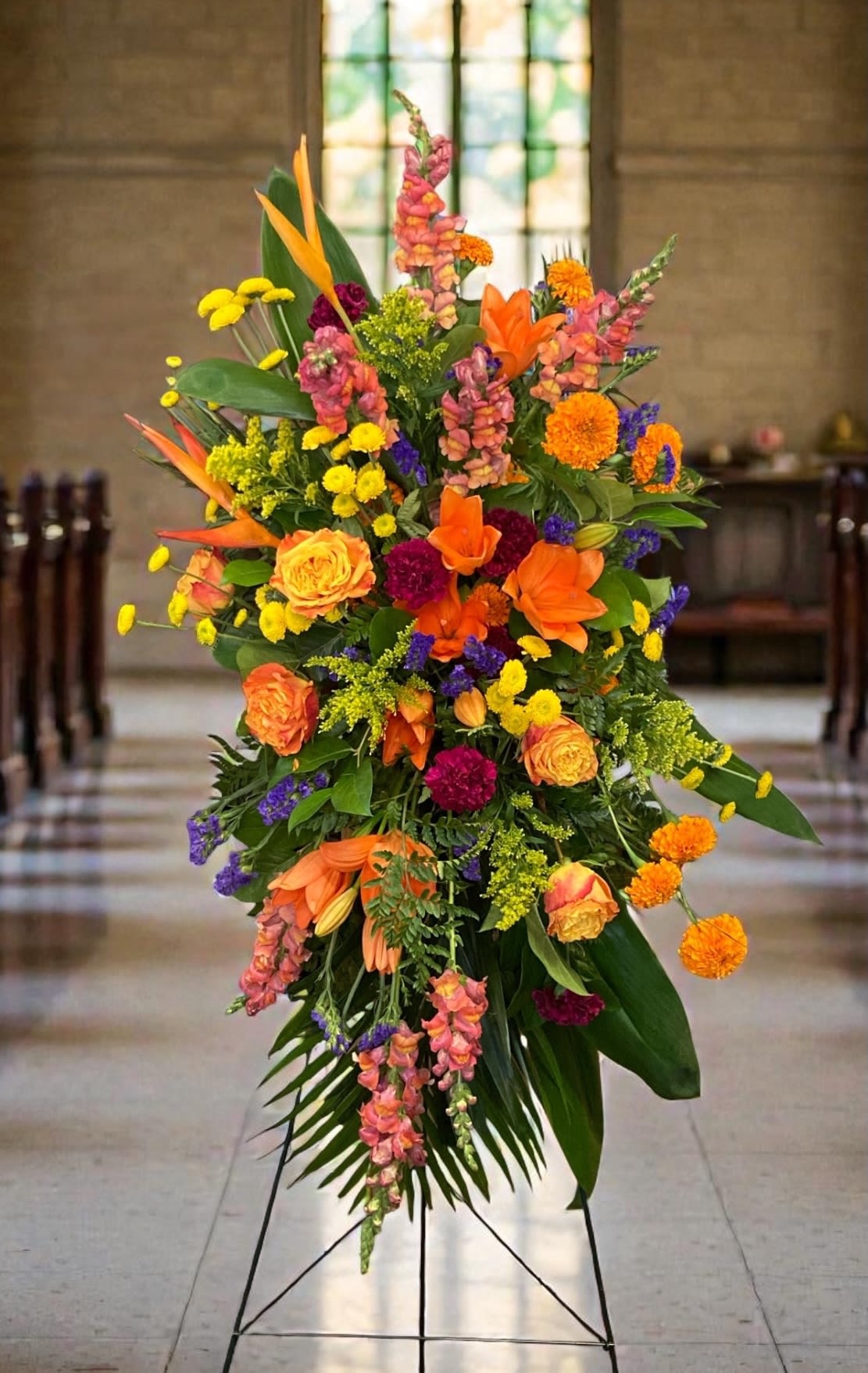 Vivid Remembrance Easel Spray - A bright, celebratory statement for a funeral, memorial service, or commemorative ceremony. This flower arrangement full of vivid oranges, yellows and purples, to capture a masculine or summer feel.