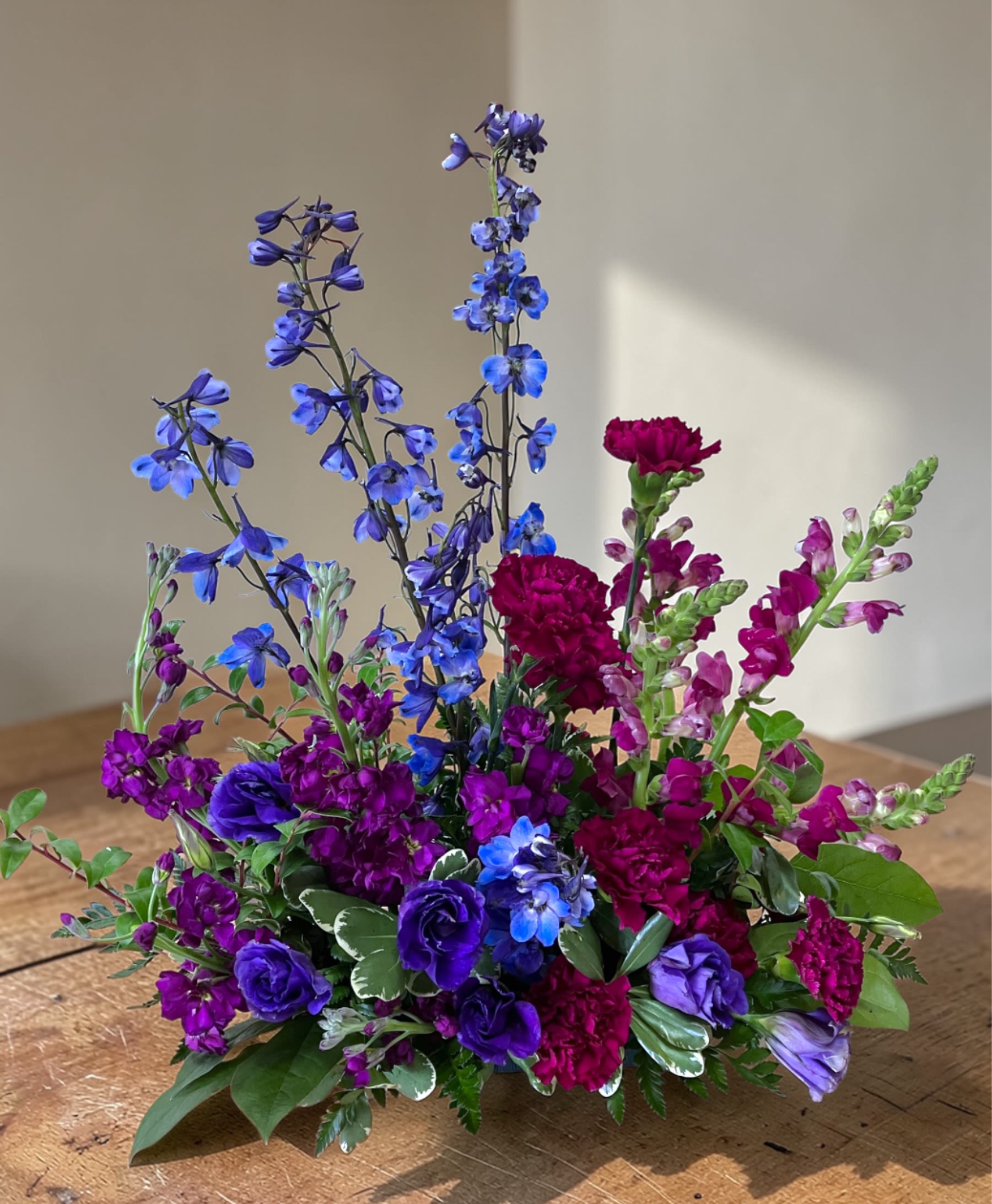 Jeweled Elegance - Tall blue delphinium give this flower arrangement a striking vertical silhouette, paired with lush clusters of purple and magenta blooms for a vivid celebration of life.