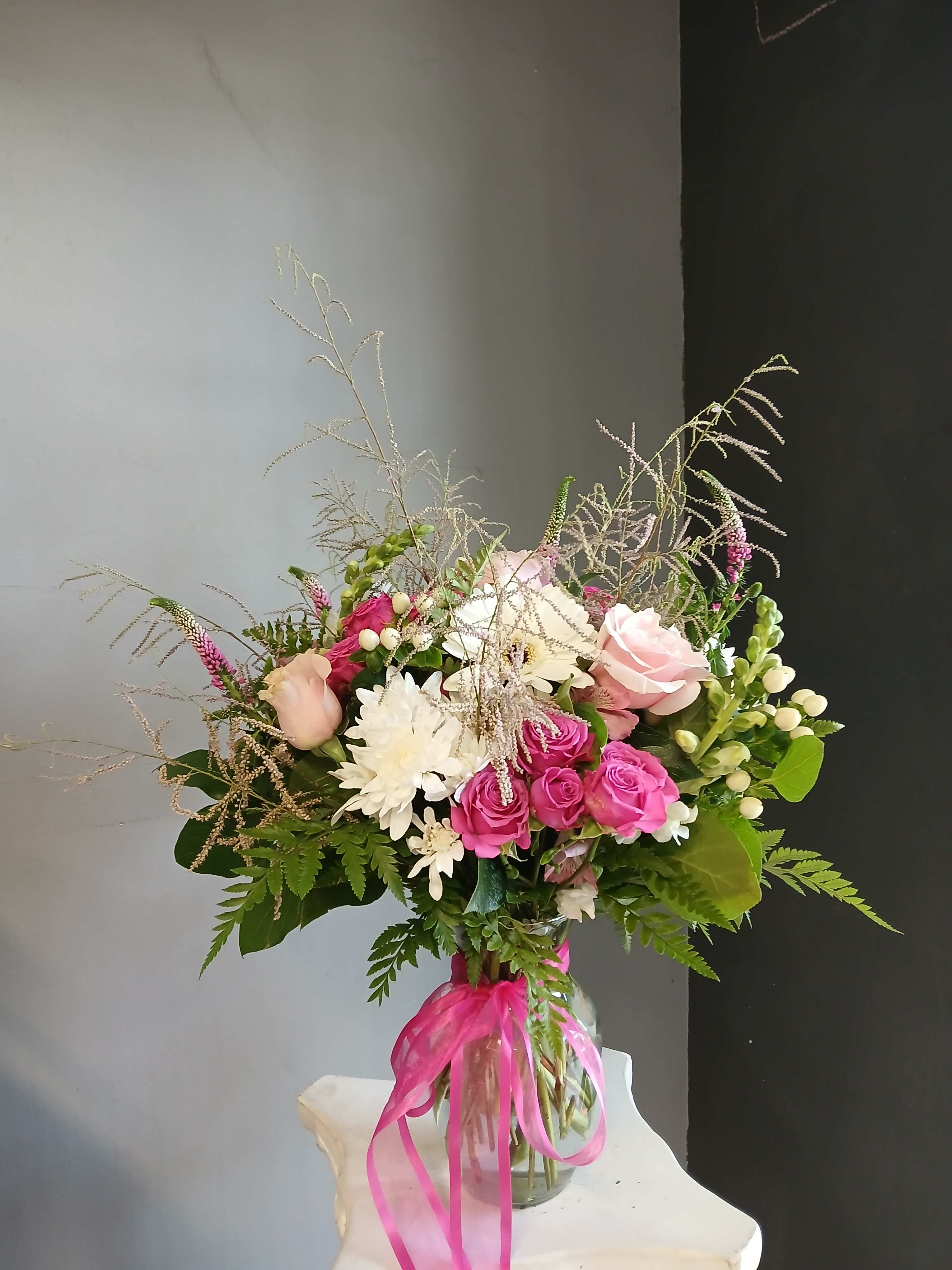 Bouquet of pink and white flowers in a glass vase with a pink ribbon