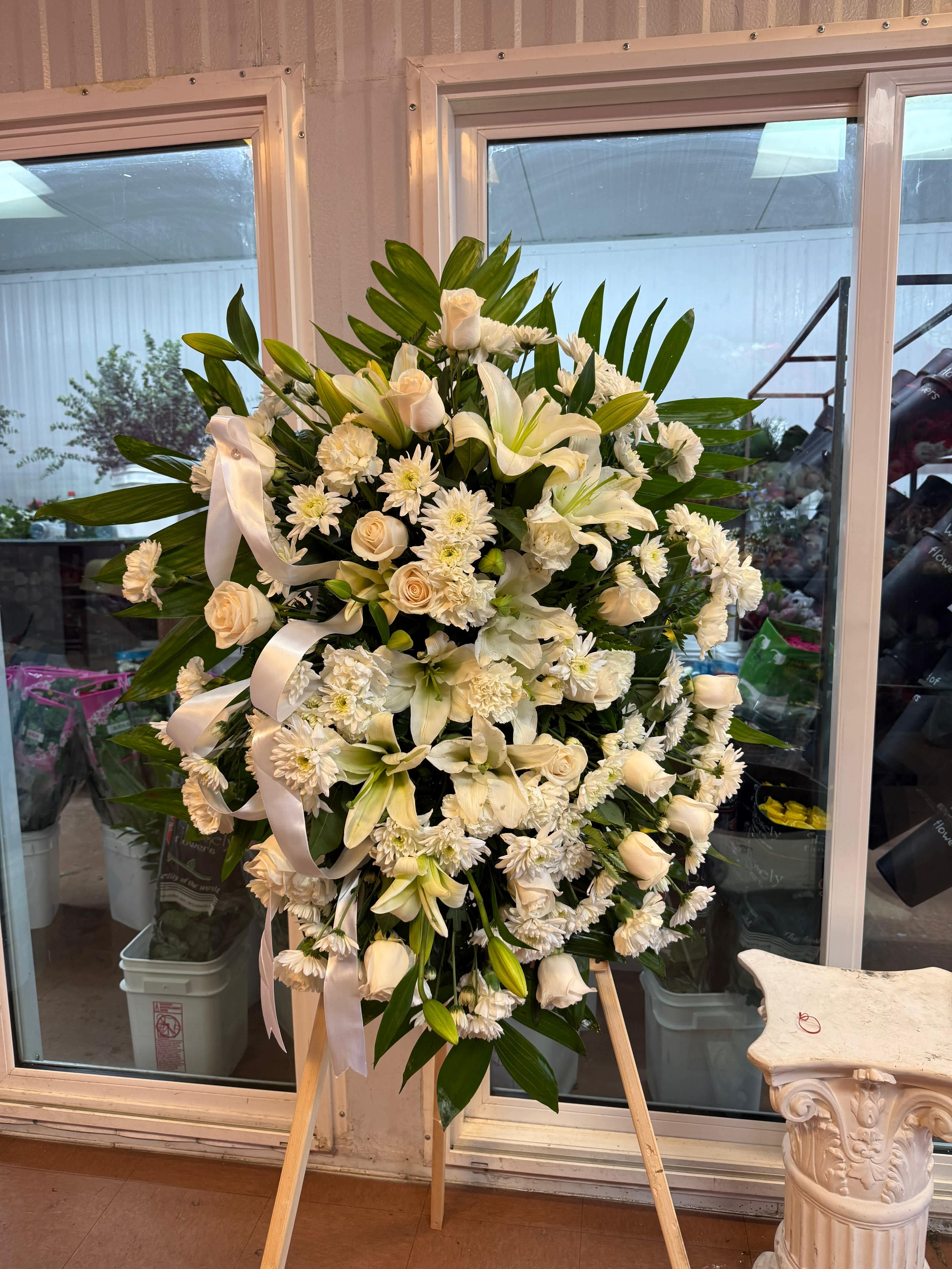 Large white funeral spray on an easel with lilies, roses, and ribbon