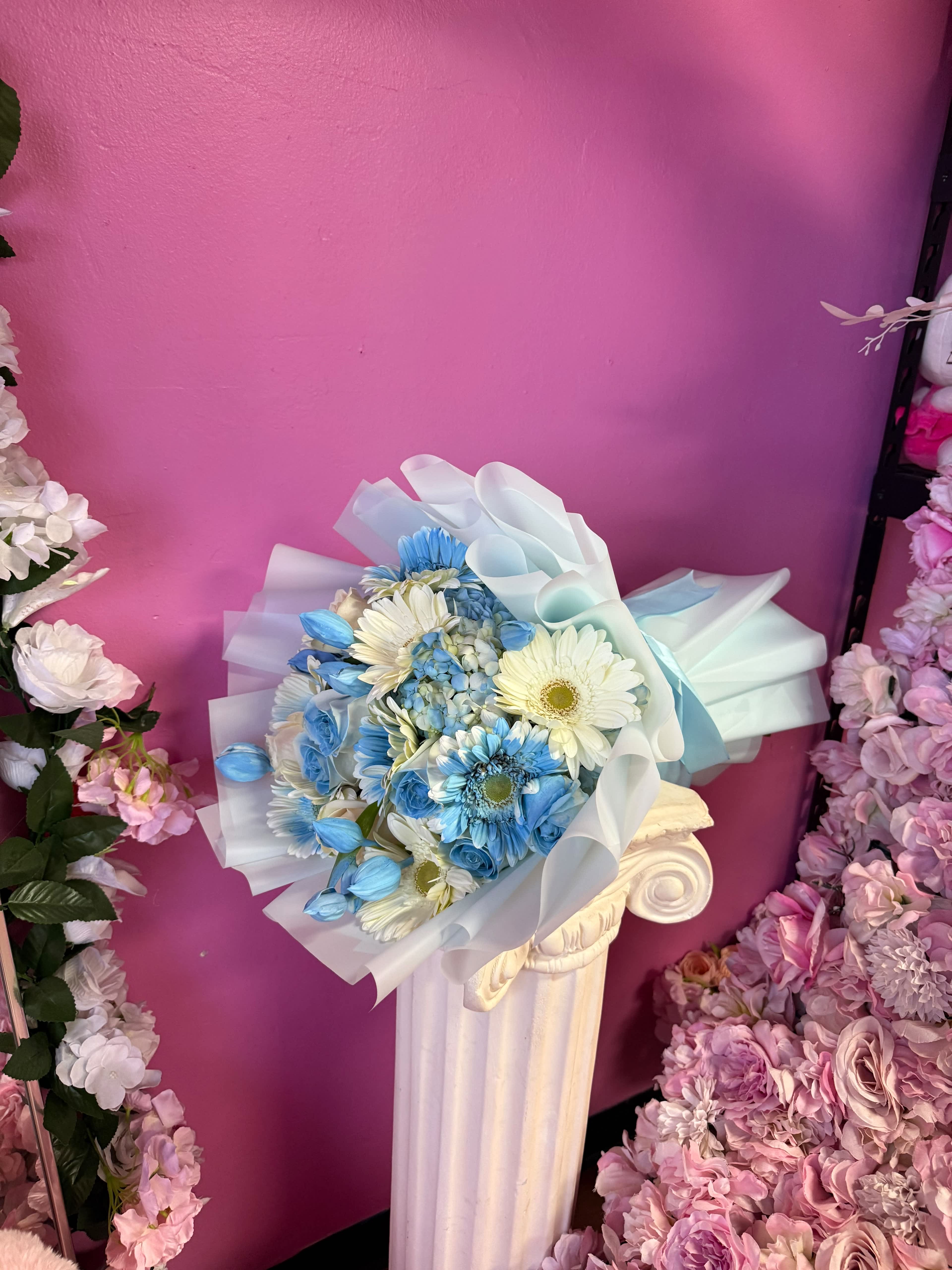 Blue and white bouquet wrapped in translucent paper on a pedestal