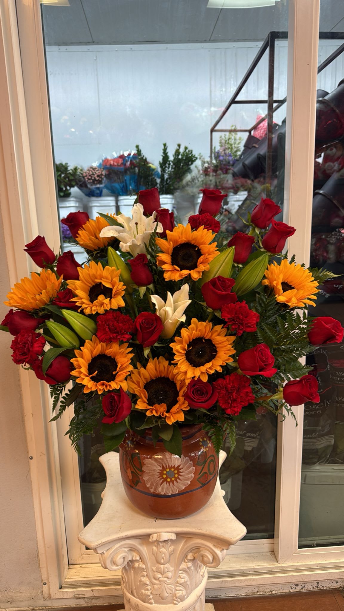 Bouquet of red roses, sunflowers, white lilies, and red carnations in a painted vase