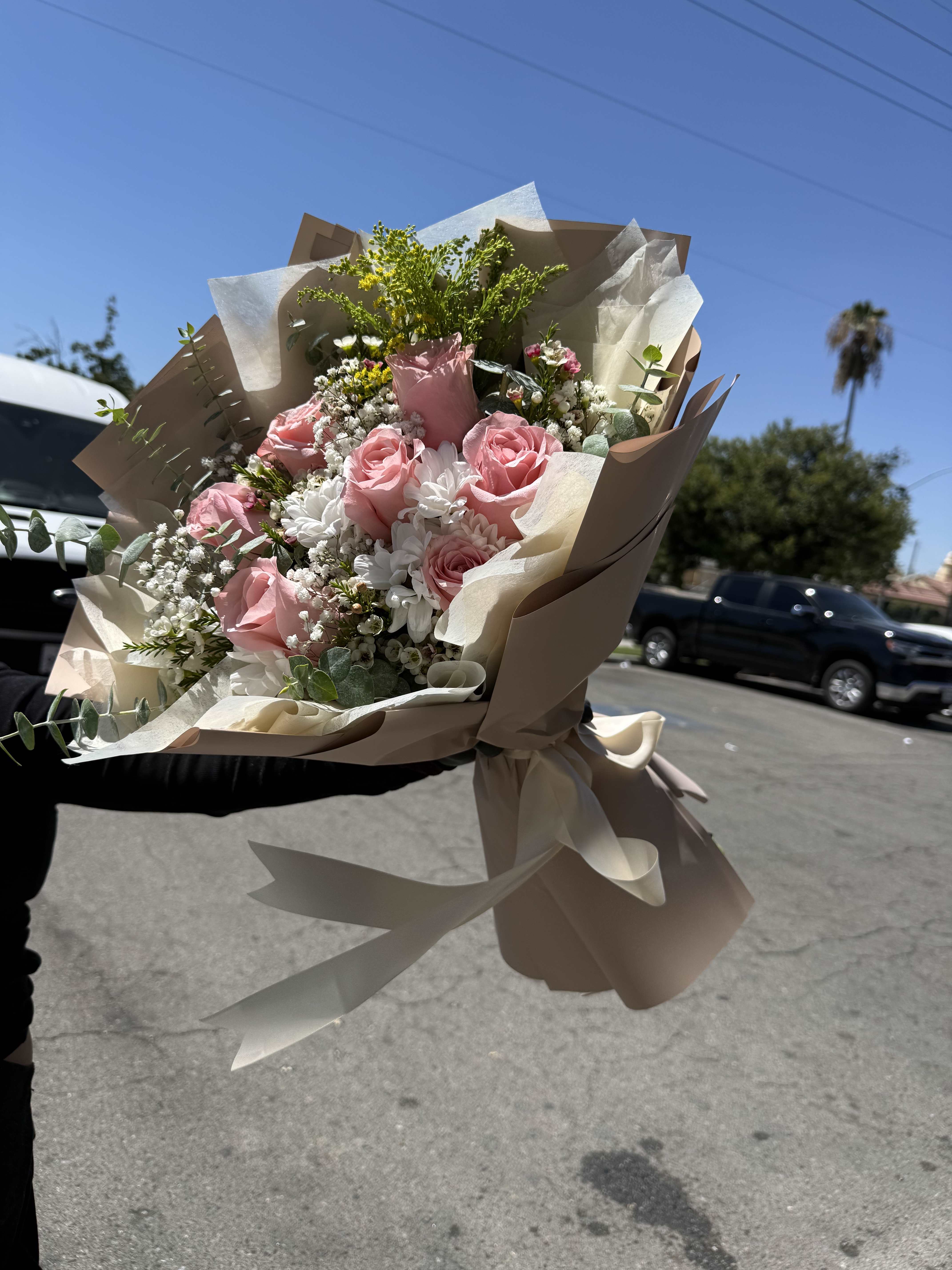 Handheld bouquet of pink roses and white flowers wrapped in beige paper
