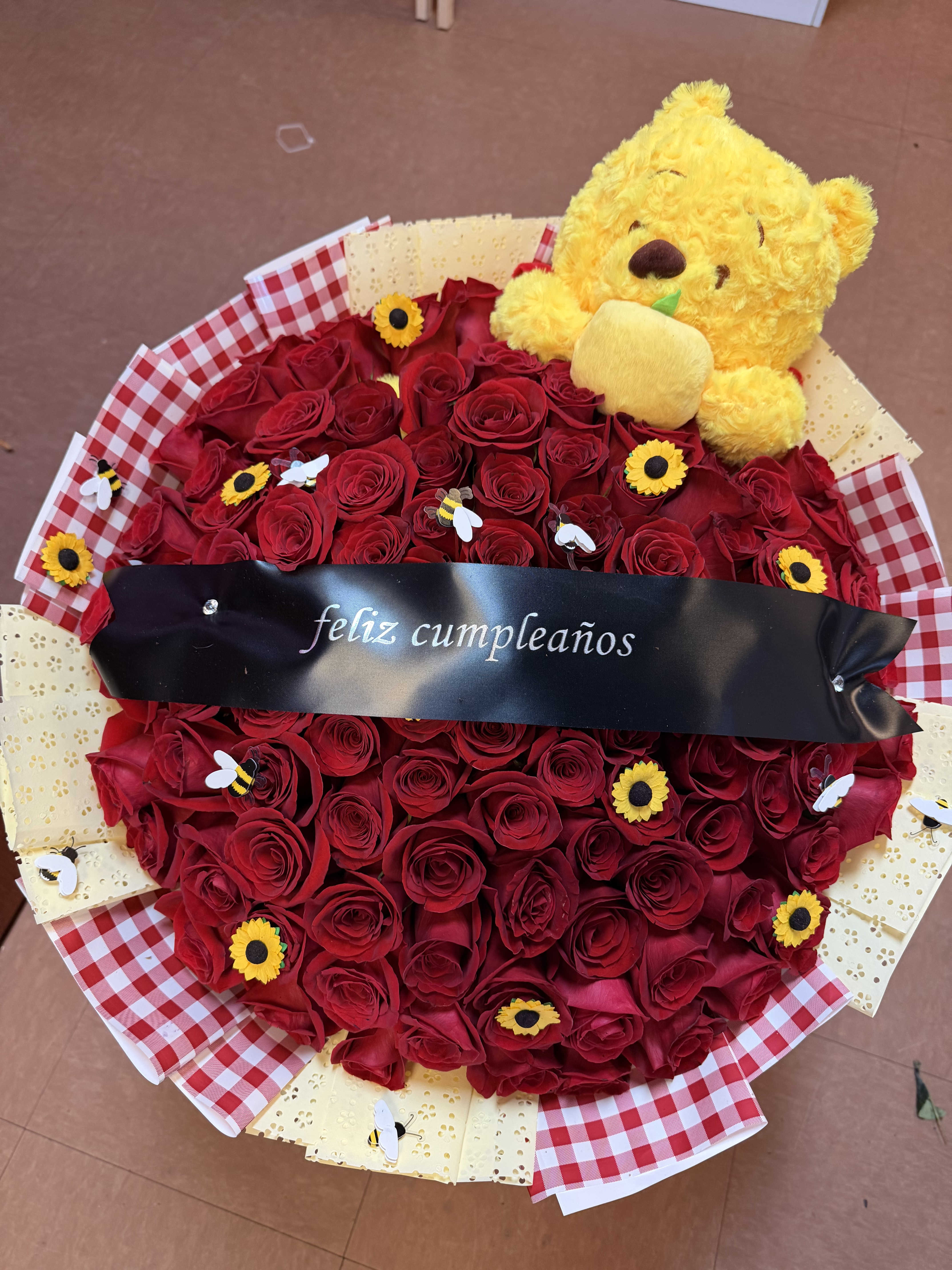 Heart-shaped bouquet of red roses with a yellow teddy bear and birthday ribbon