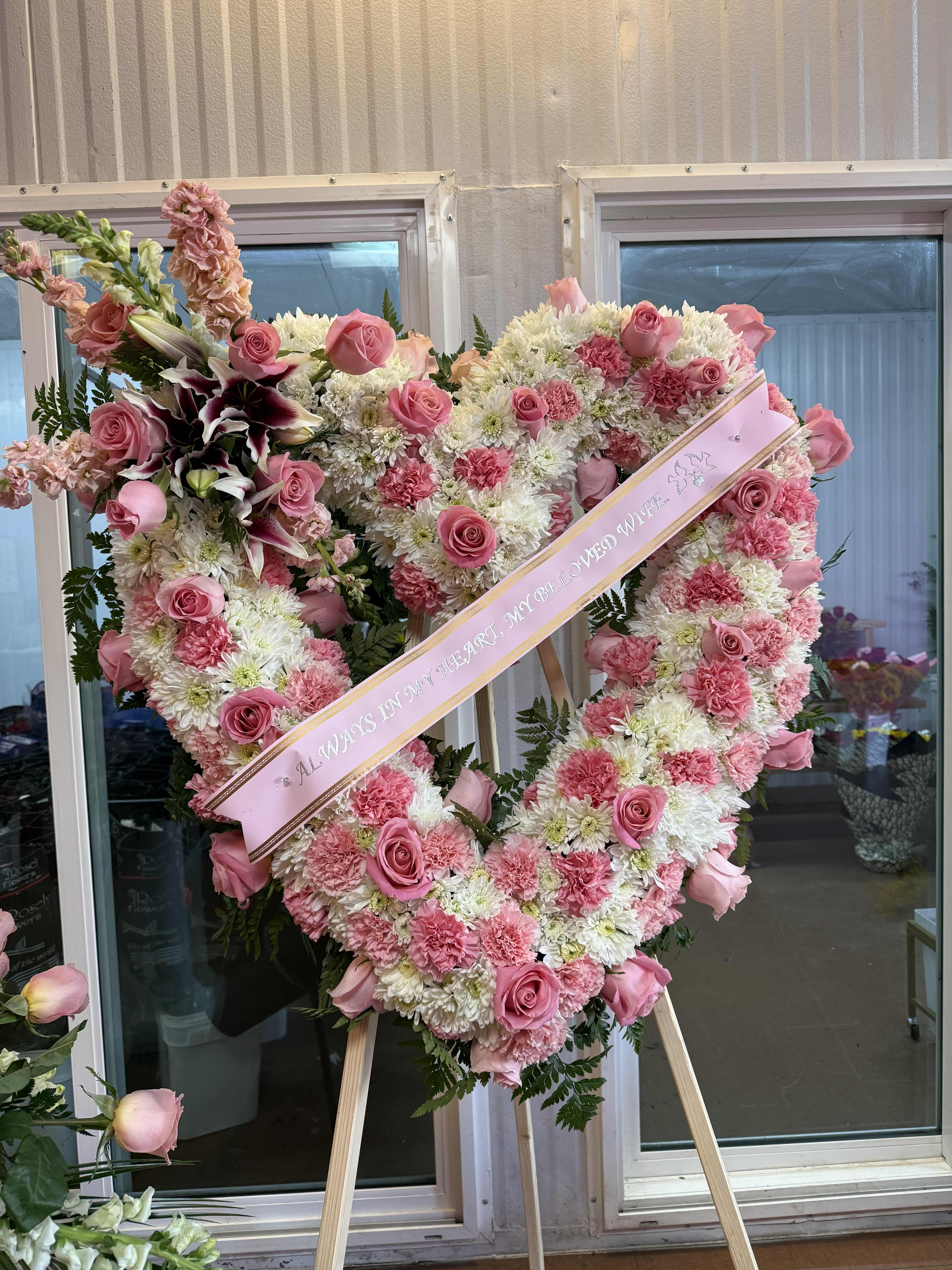 Heart-shaped pink and white floral standing spray with a ribbon across it