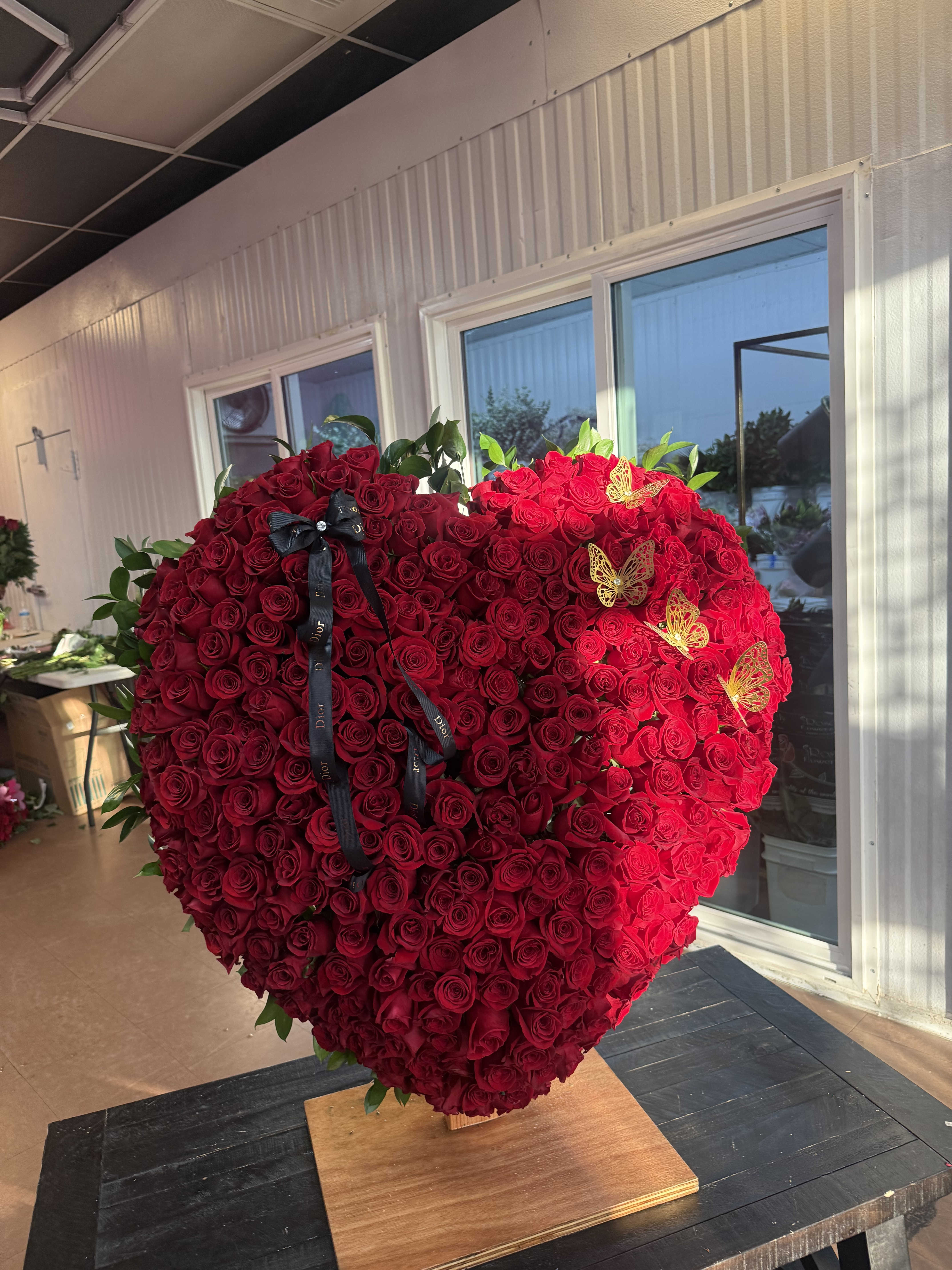 Large heart-shaped arrangement of red roses with a black ribbon and gold butterfly accents