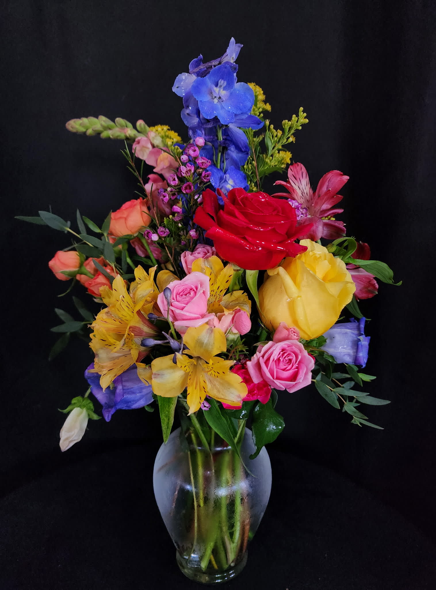 Colorful mixed bouquet in a frosted glass vase with roses and lilies