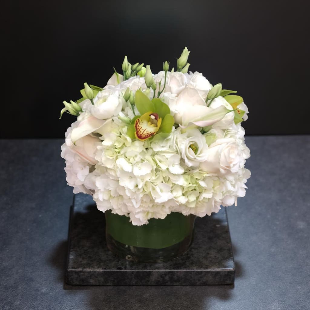 White floral arrangement in a glass vase with green accents