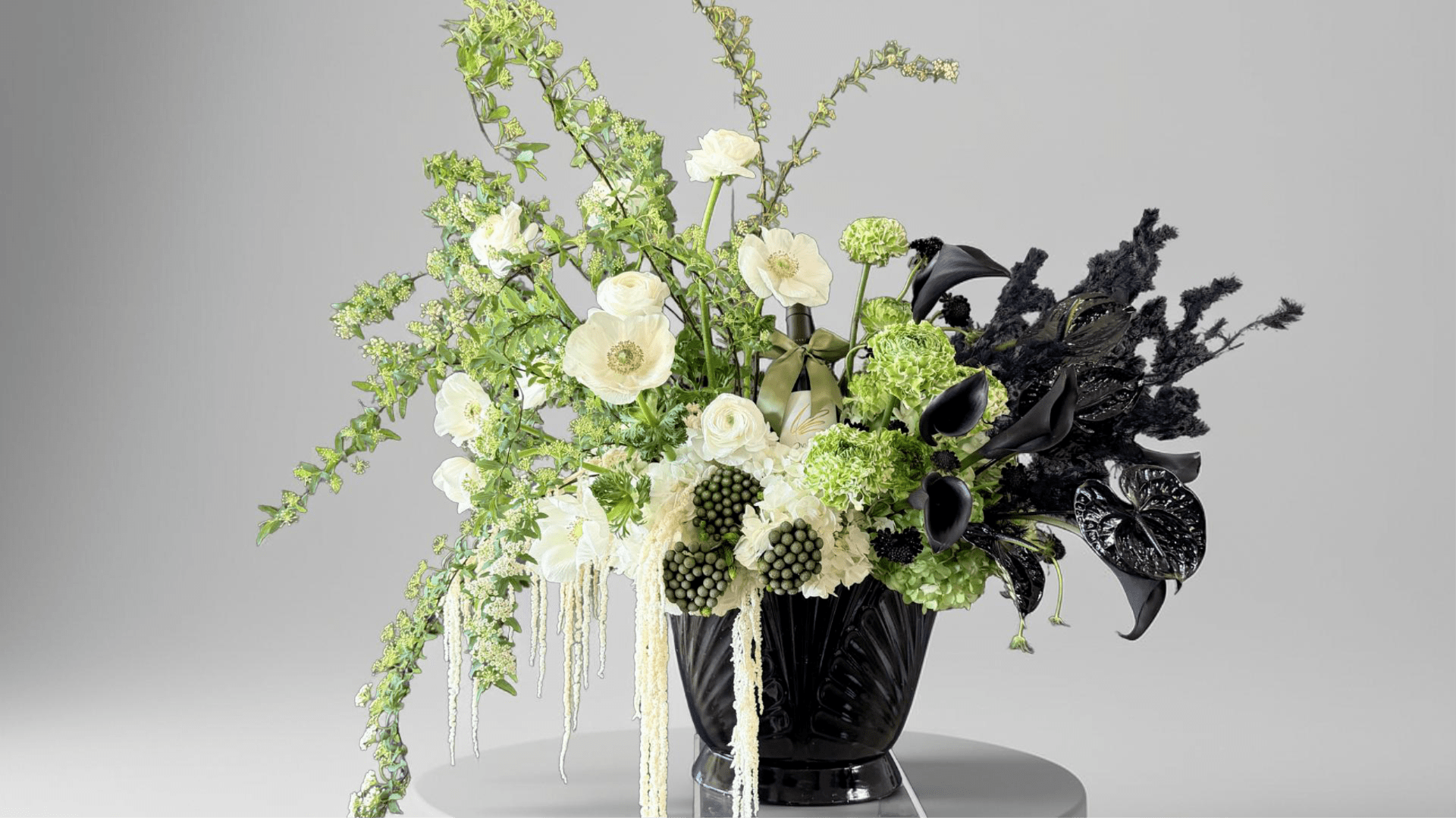 Black vase with white and green floral arrangement and black calla lilies