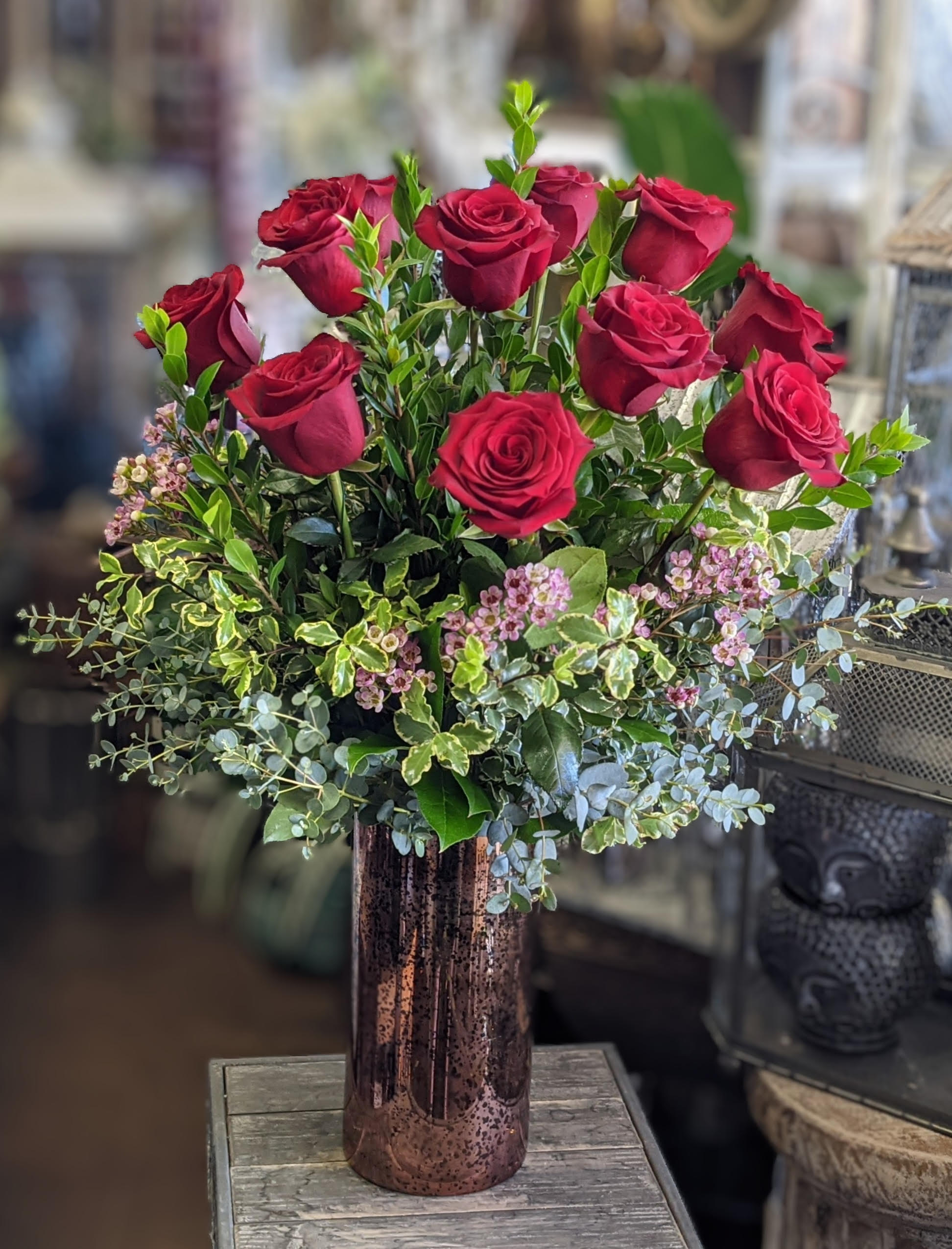 Red roses arranged in a tall copper vase with mixed greenery