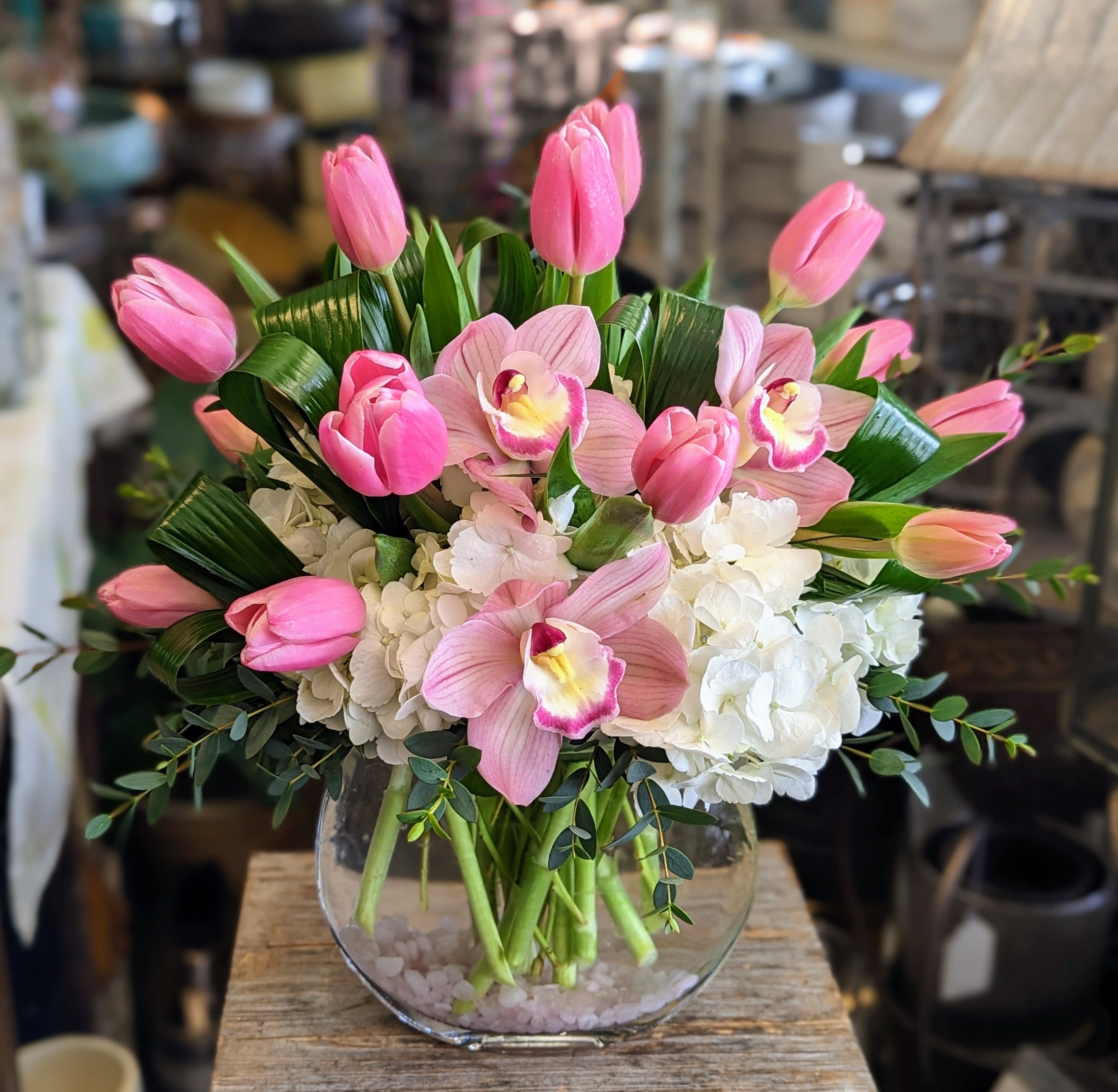 Pink tulips and orchids arranged in a clear glass vase with white hydrangeas.
