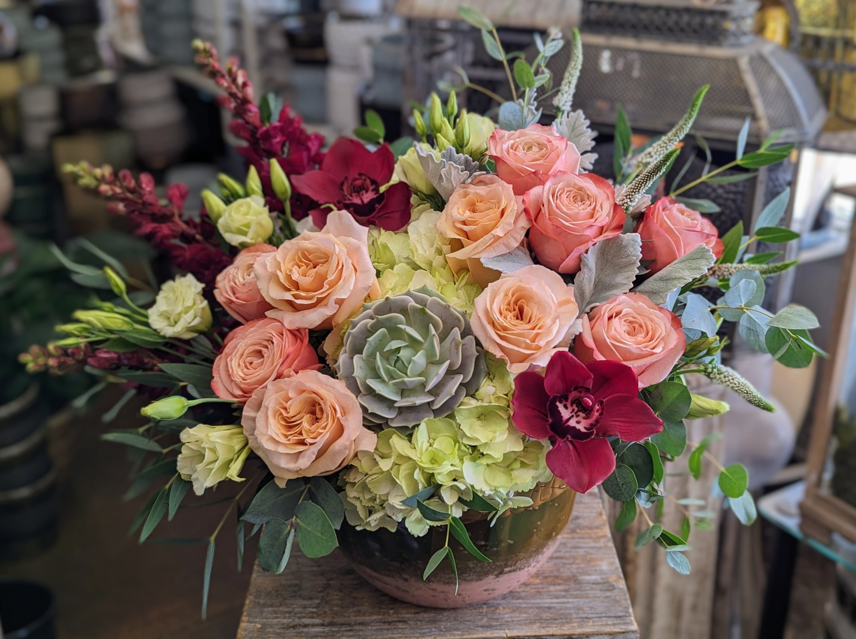 Peach and pink roses with burgundy orchids in a low bowl arrangement