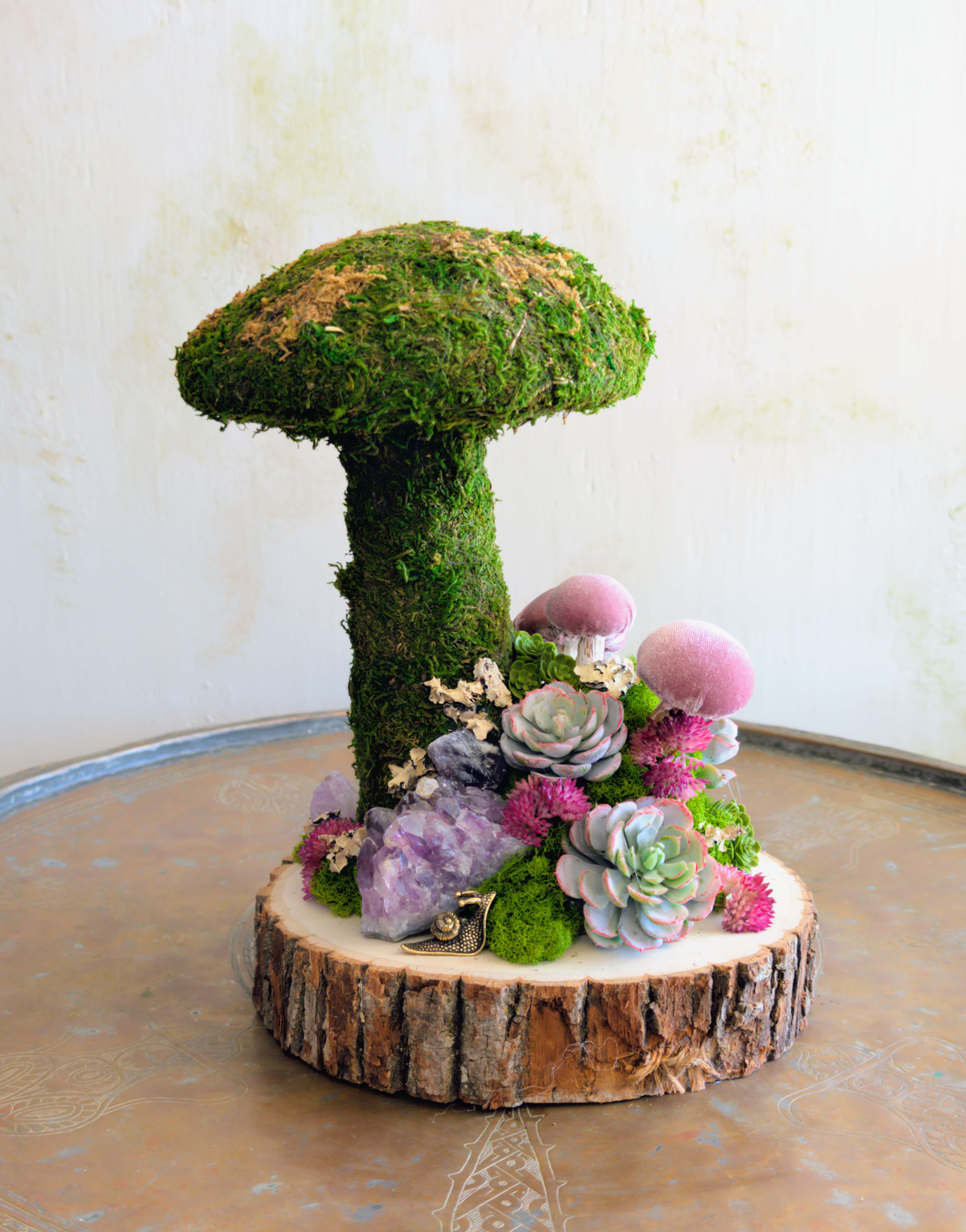 Moss-covered mushroom-shaped arrangement with succulents and crystals on a wood slice base