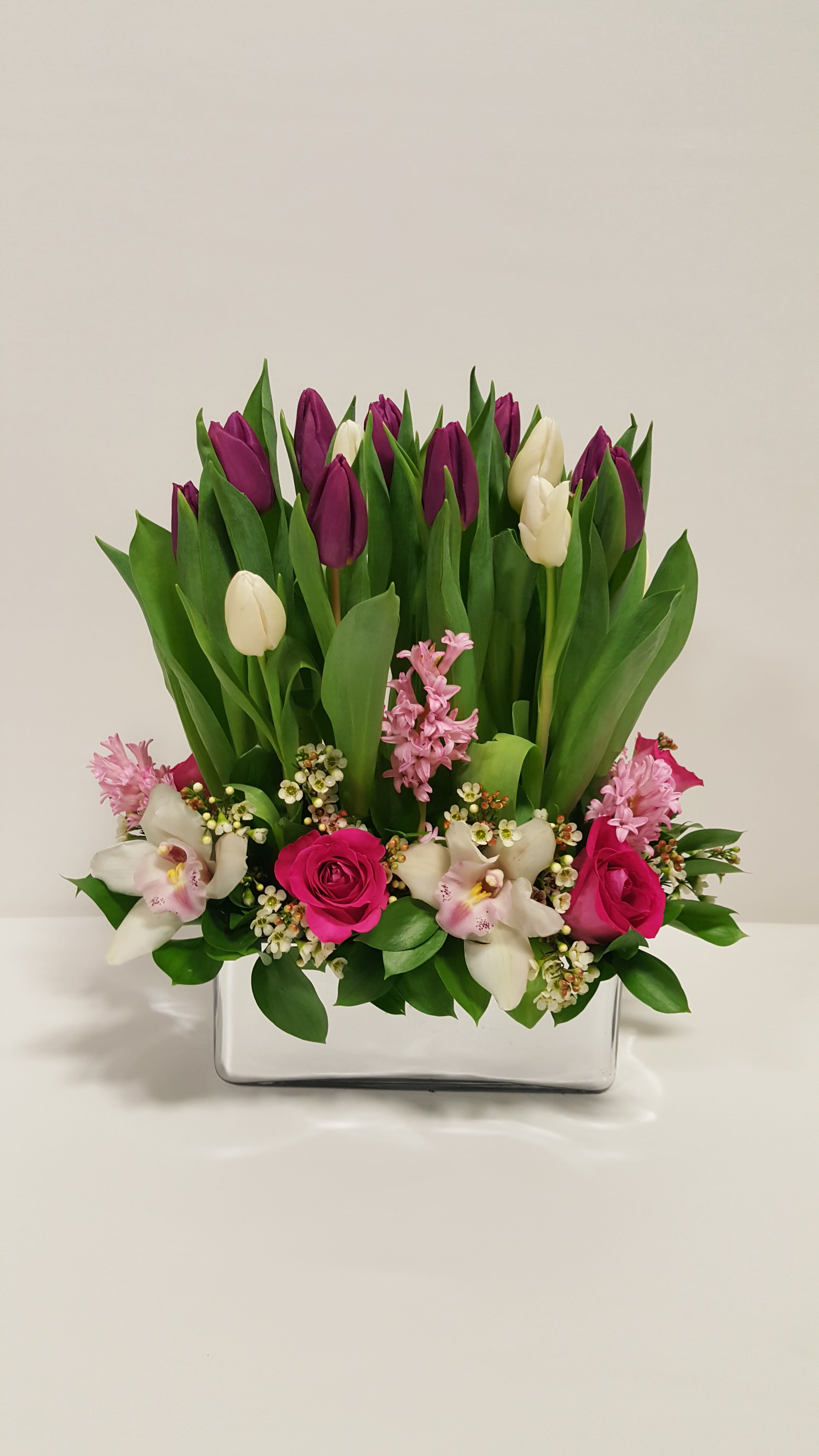 Make a Wish - This lovely design comes in a silver rectangular vase well arranged with some White and Purple tulips standing up mix with pink roses, pink hyacinth, White cymbidium orchid, touch of wax and greenery. Perfect for  birthday flowers anniversary flower  just because flowers  congratulations flowers  Get well flowers  Christmas flowers Valentines Day flowers Mother's Day flowers  