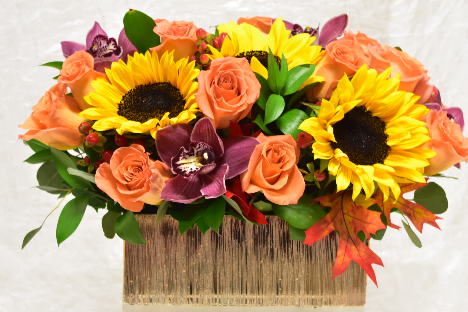 Sunflowers and peach roses in a rectangular vase with purple orchids