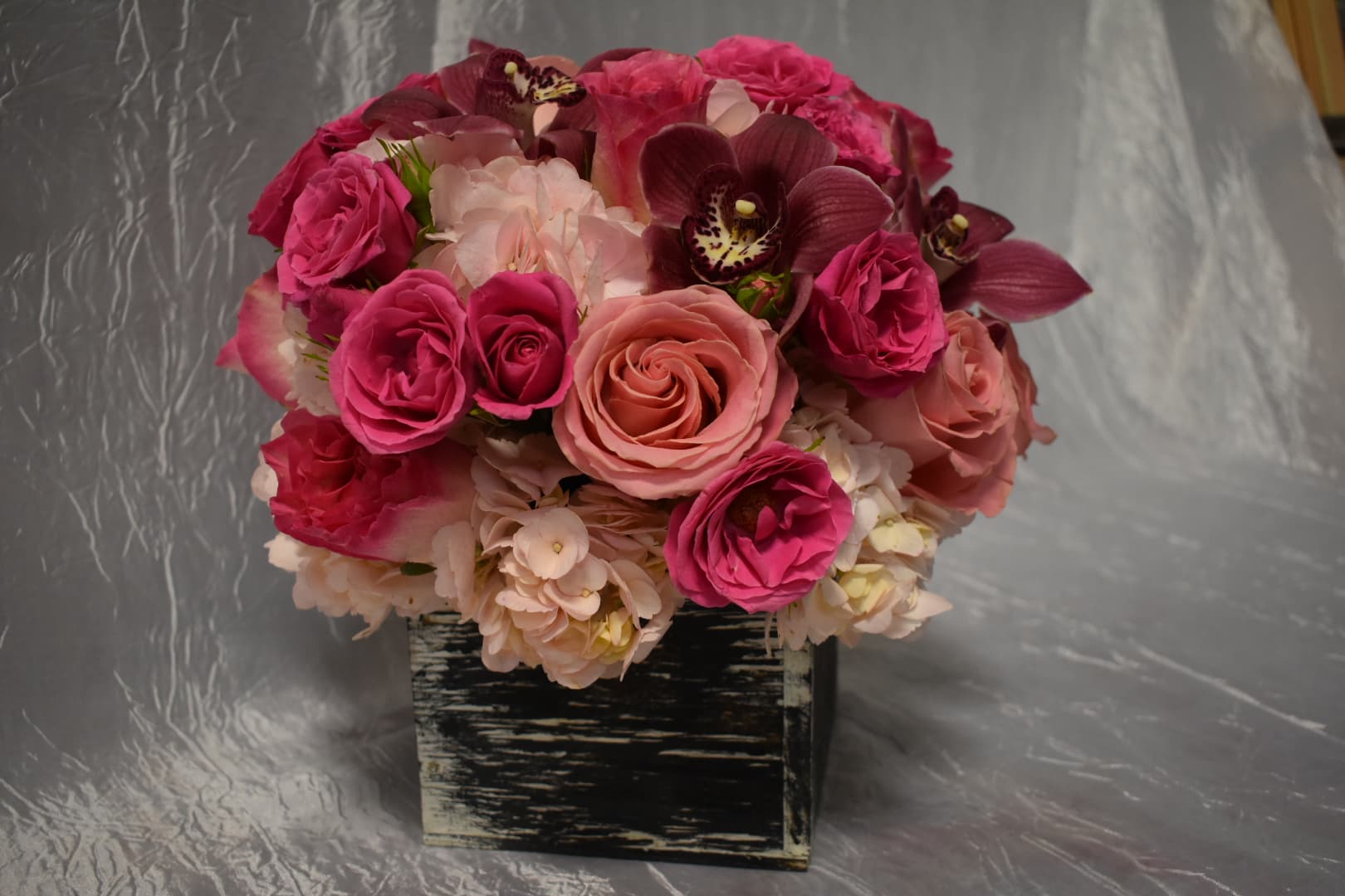 Pink and peach roses with orchids in a black square container