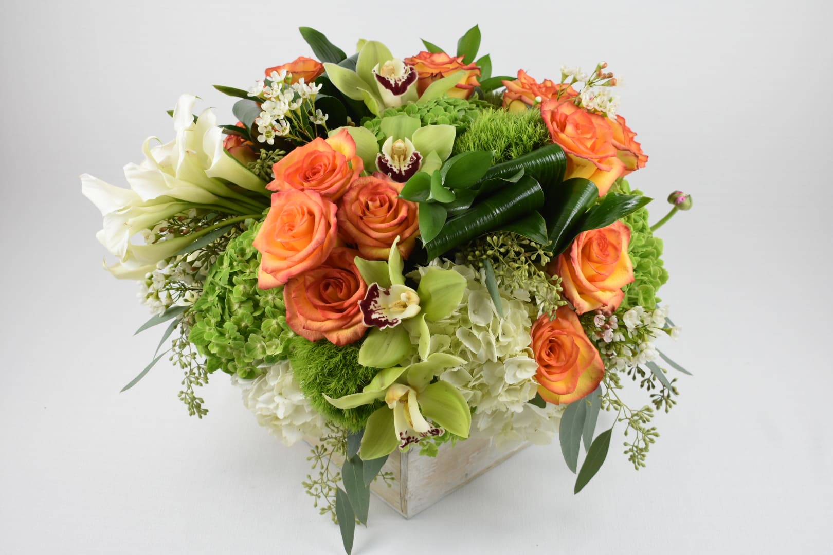 Orange roses and white lilies arranged in a square vase