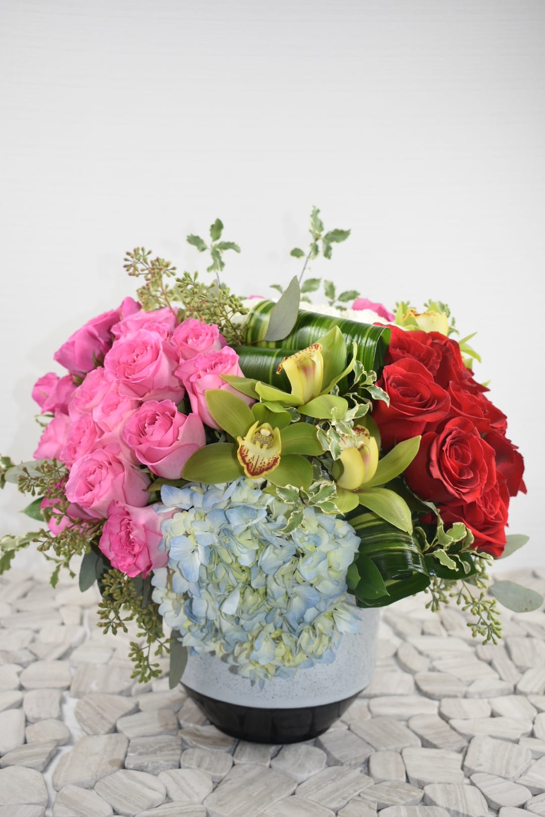 Pink and red roses with blue hydrangea and green orchids in a vase